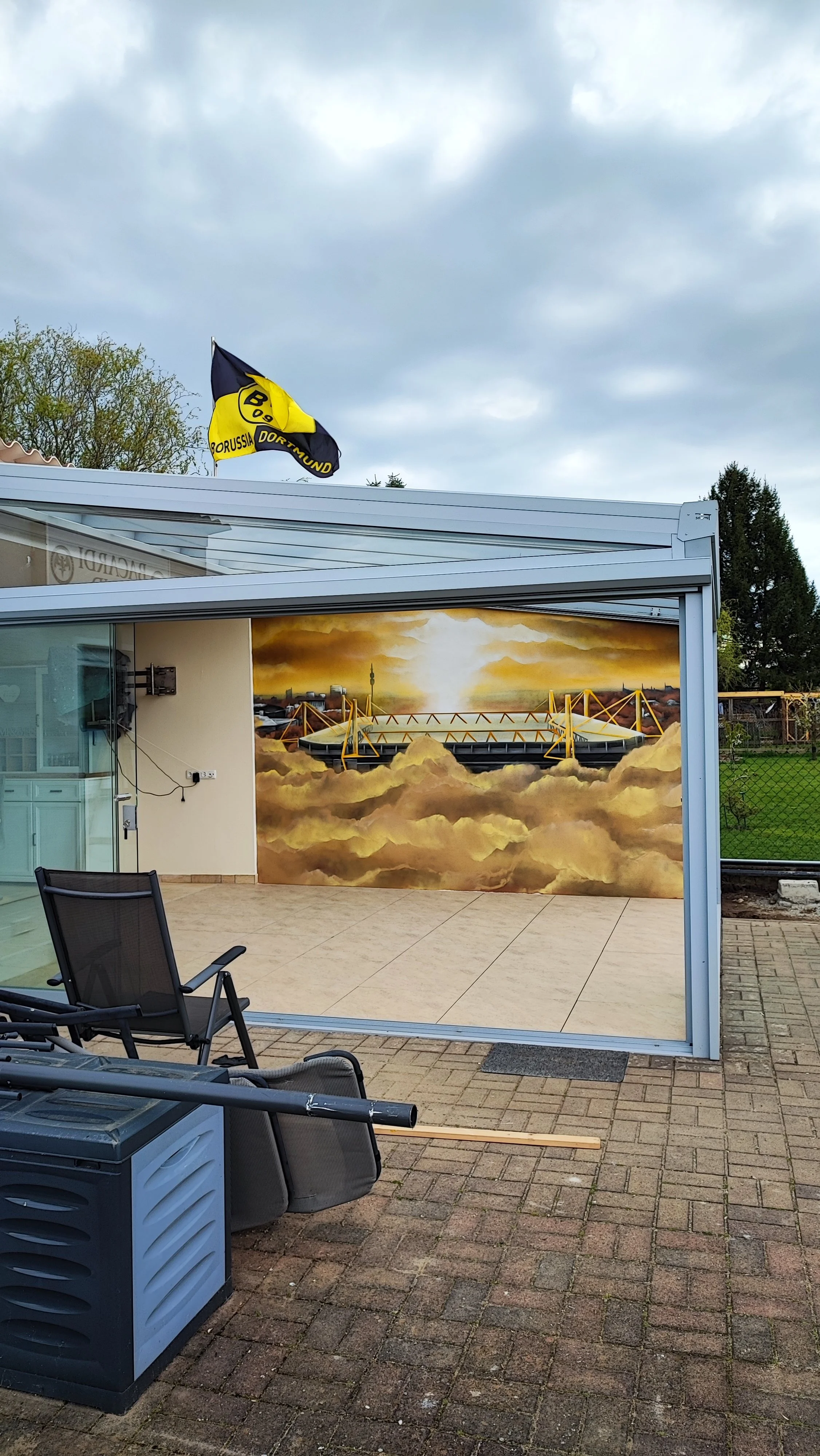 Eine Wandmalerei zeigt eine Brücke in den Wolken, mit einem Sonnenaufgang oder Sonnenuntergang im Hintergrund, im Innenraum eines Gebäudes.