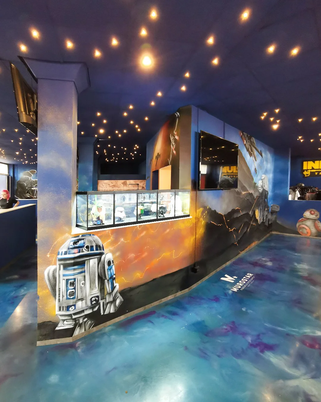 Star Wars thematischer Raum mit Wandmalerei, R2-D2 Figur und interaktiven Bildschirmen, inspiriert von Star Wars Filmen.