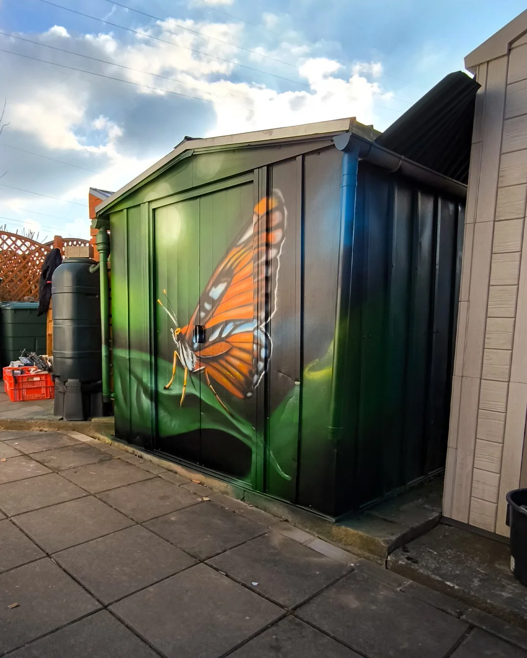 Graffitimalerei einer orangefarbenen Schmetterlings auf einer schwarzen Gartenhütte