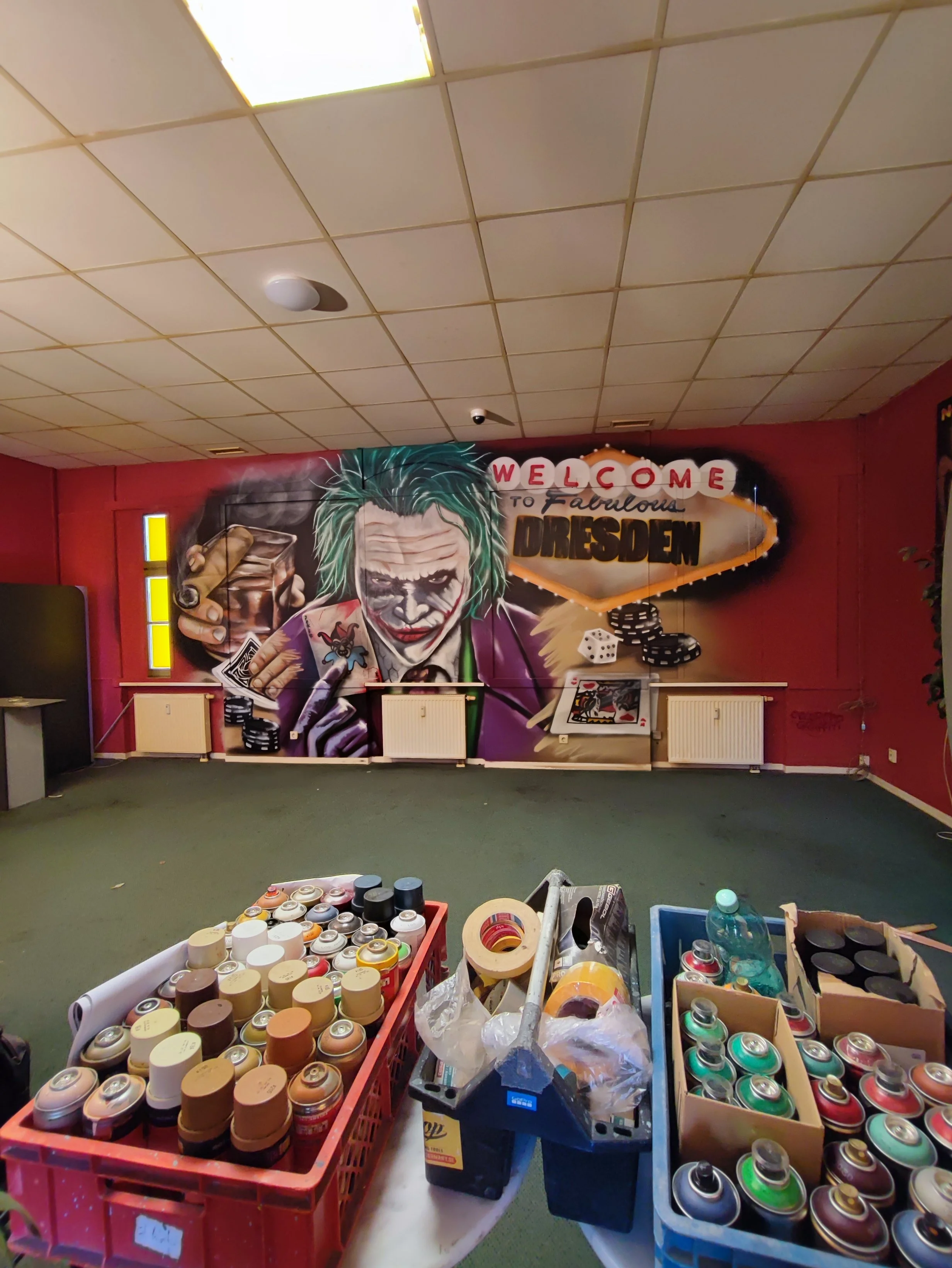 Graffiti Wandbild des Jokers in einem Raum mit Spraydosen auf Tischen, dekoriert mit einem Willkommen-Schild in Dresden.