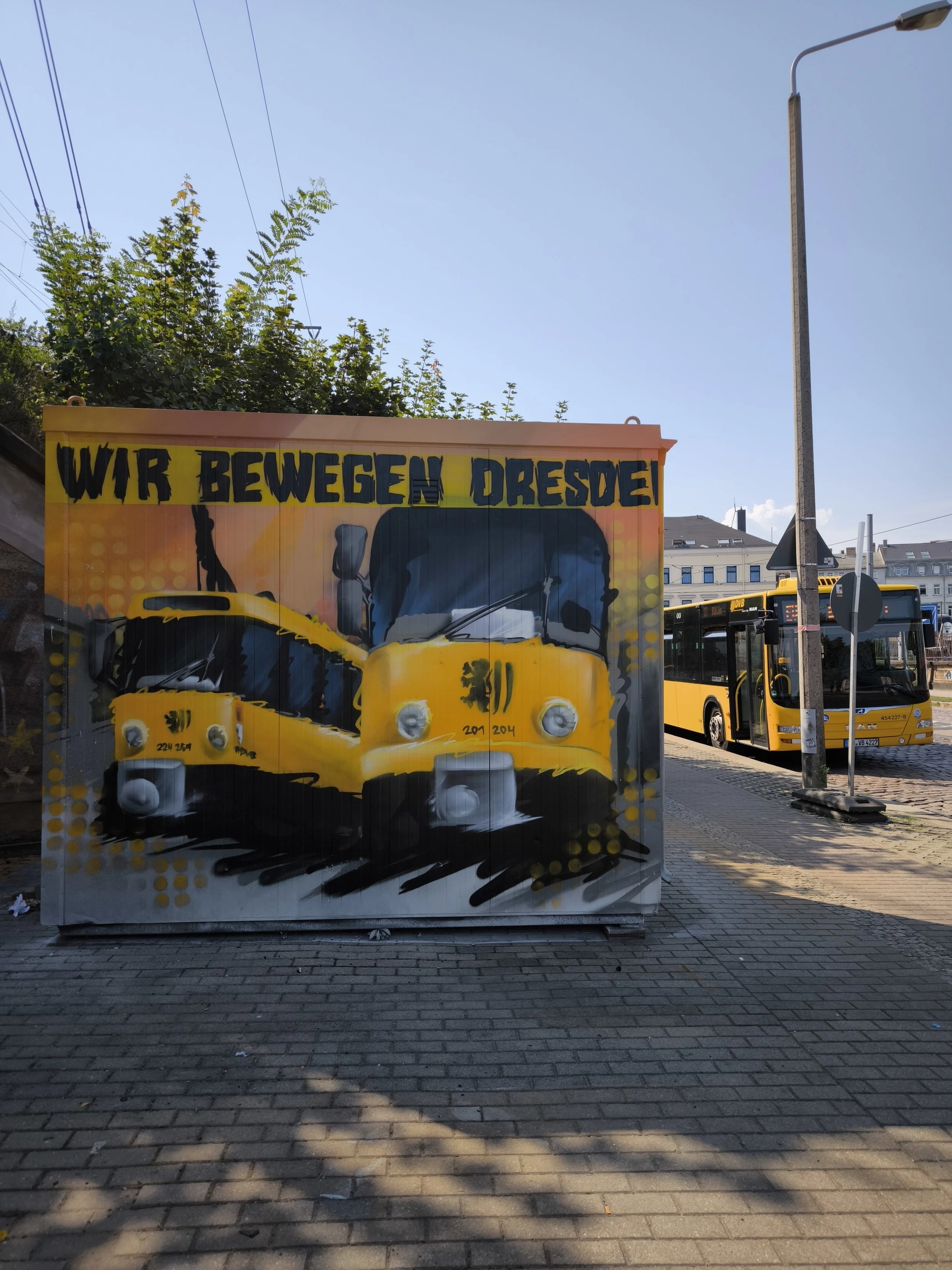 Graffiti auf einer Wand mit einem Bus und der Aufschrift "Wir bewegen Dresden". Im Hintergrund sind weiteres Transportmittel und Gebäude sichtbar. Professionelle Graffitigestaltung in Dresden: individuelle Wandgestaltung, Auftragsgraffiti sowie kreat