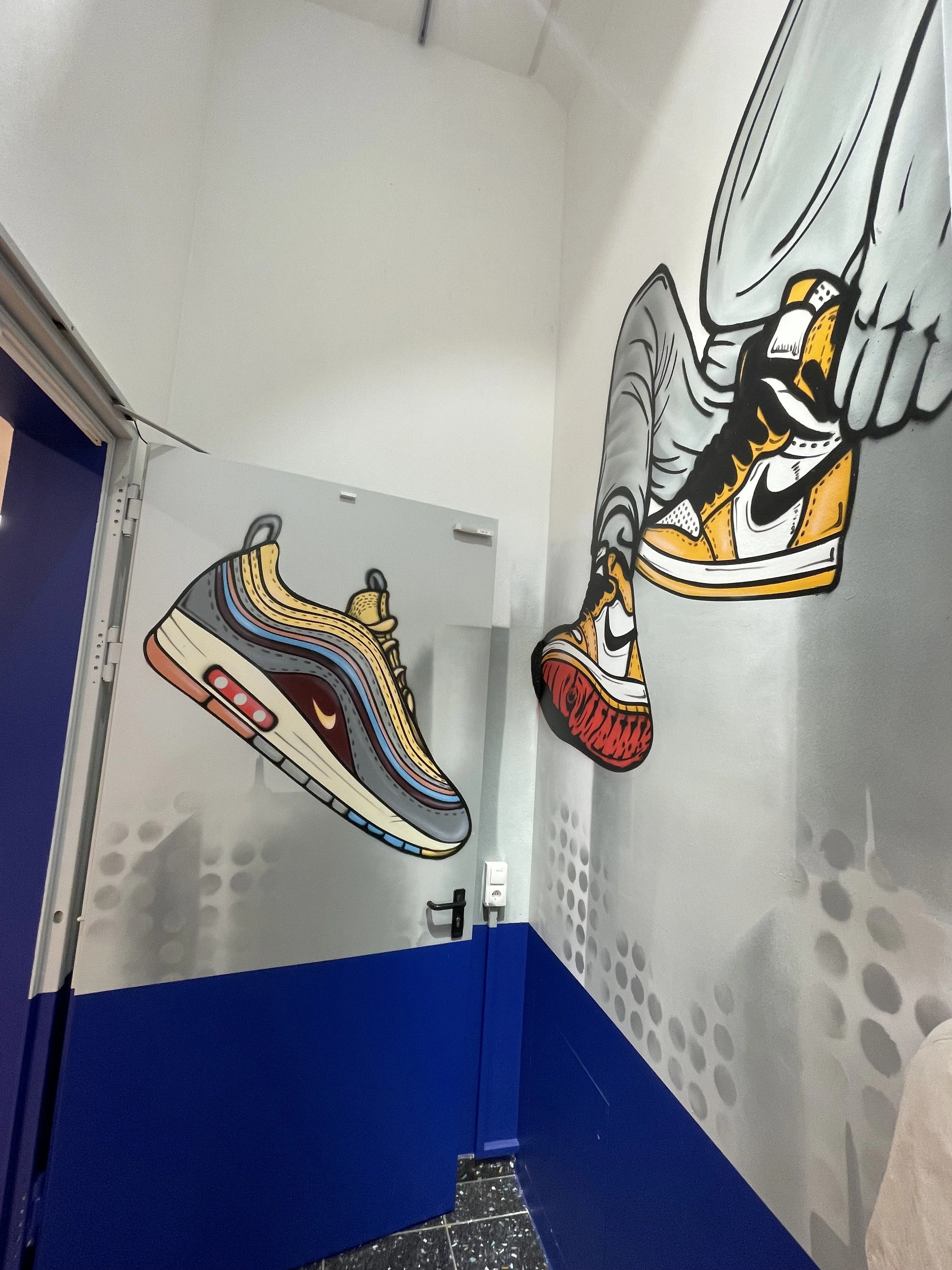 Wandkunst mit großen, stilisierten Sneakers, die an der Wand entlang laufen, in einer modernen, urbanen Umgebung.