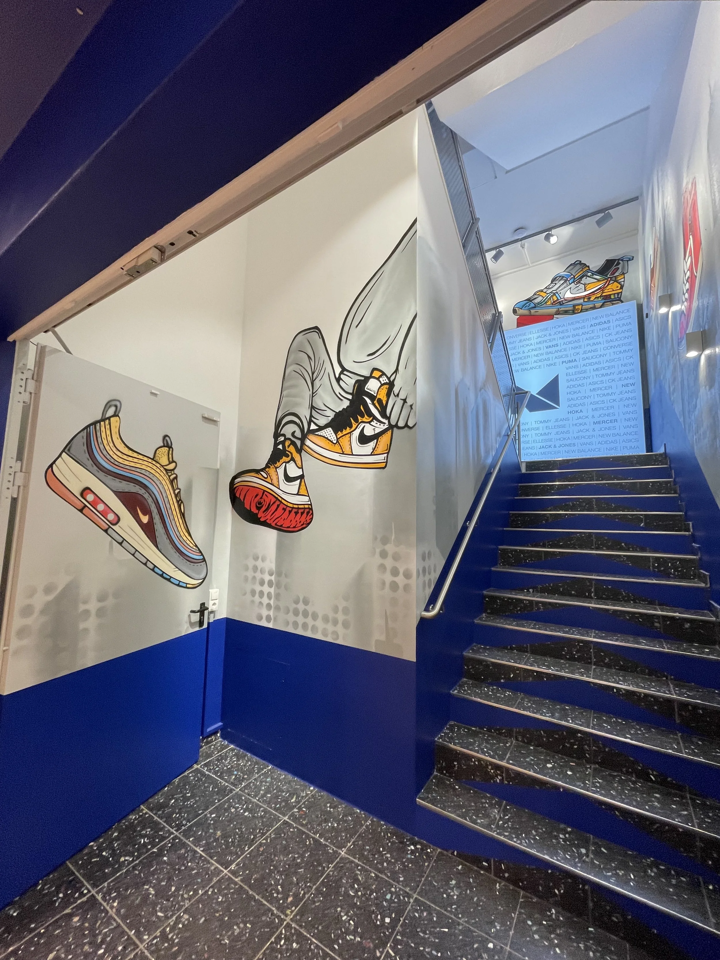 Mural mit Sneakers und einer Person, die Schuhe trägt, in einem Treppenhaus