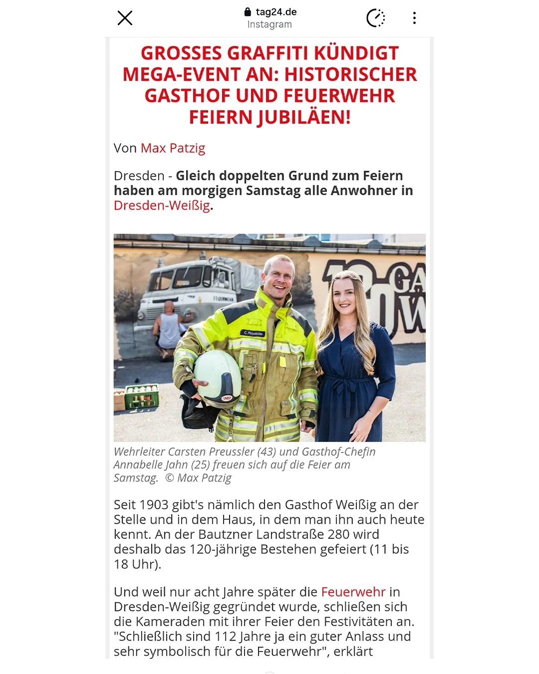 Ein Feuerwehrmann und eine junge Frau stehen vor einer Wand mit Graffiti. Der Feuerwehrmann trägt eine leuchtend gelbe Schutzjacke und hält einen Helm in der Hand, während die junge Frau in einem blauen Kleid lächelnd neben ihm steht.