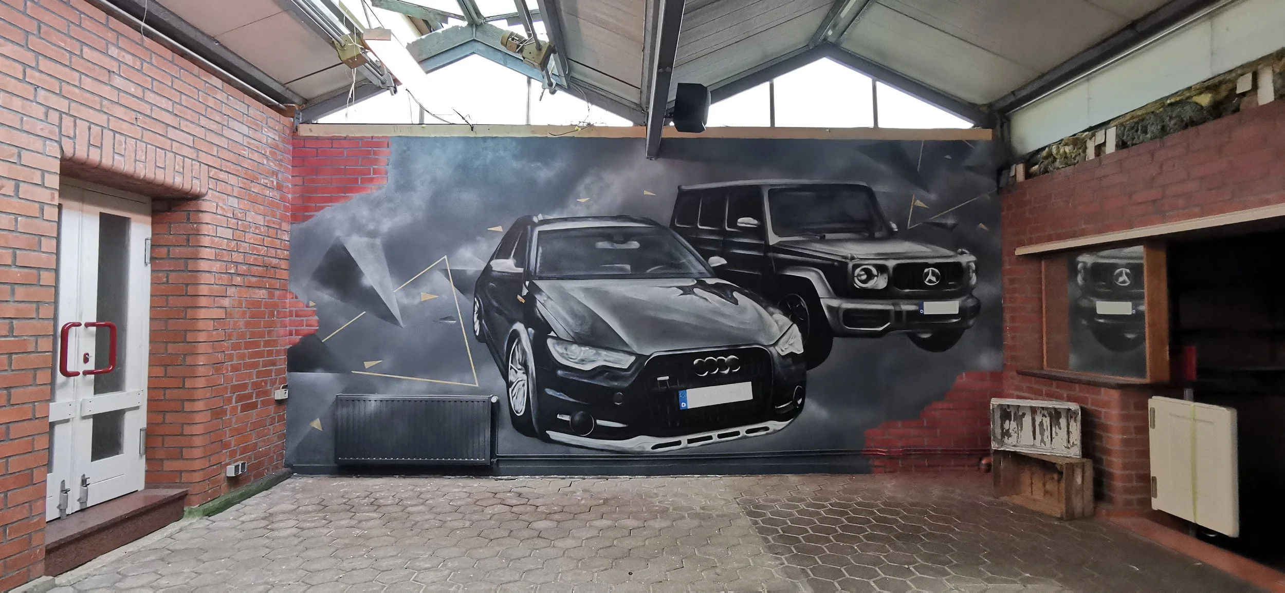 Wandmalerei mit drei schwarzen Mercedes-Benz Autos vor dunklem Hintergrund, in einem indoor Bereich mit Ziegelwänden und Holzregalen.