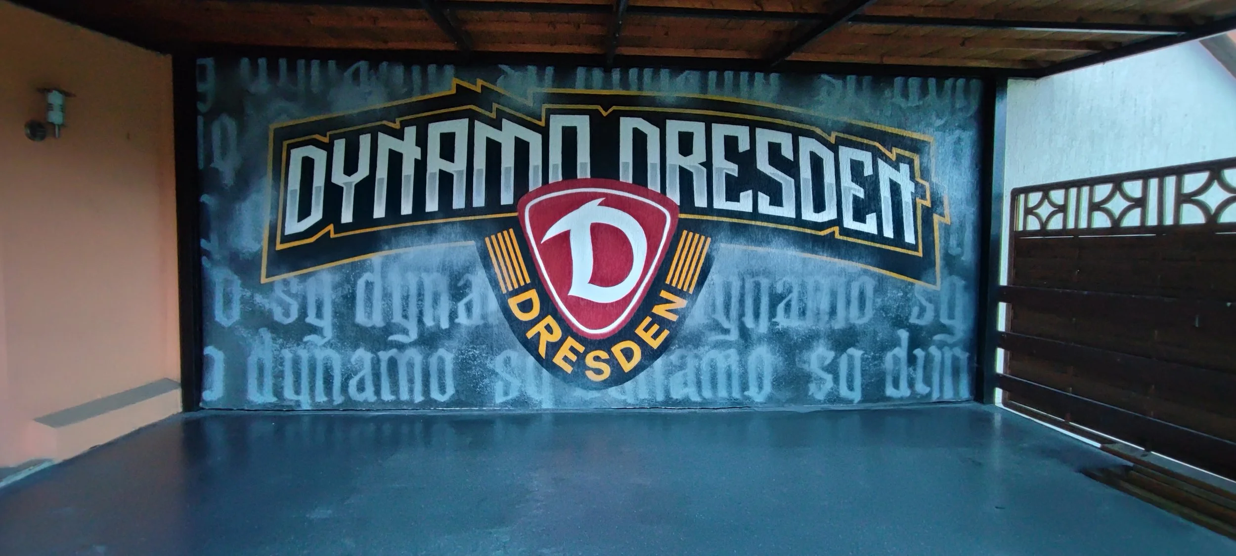 Grafik mit Text 'Dynamo Dresden' und einem rot-weißen Wappen auf einer Wand, umgeben von graffitiähnlichem Design.