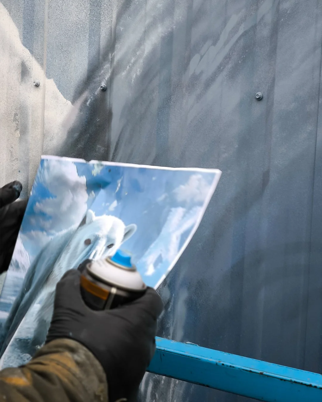 Person beim Sprayen eines Wandbildes mit einem Polar-Bär auf einer Cloud- und Himmelsszene.