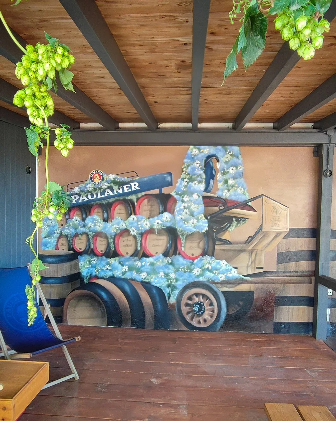 Gemälde einer Ochsenkutsche, die mit Hopfendolden und Weißdorn dekoriert ist, auf einer Holzveranda