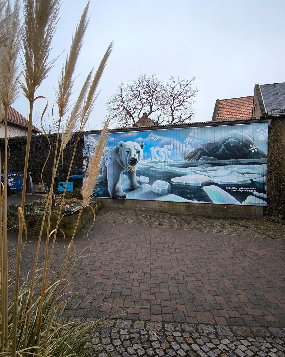 Wandgemälde eines Polarbären in einer winterlichen, arktischen Landschaft mit Eis und Bergen, auf einem Zaun in einer Außenanlage.
