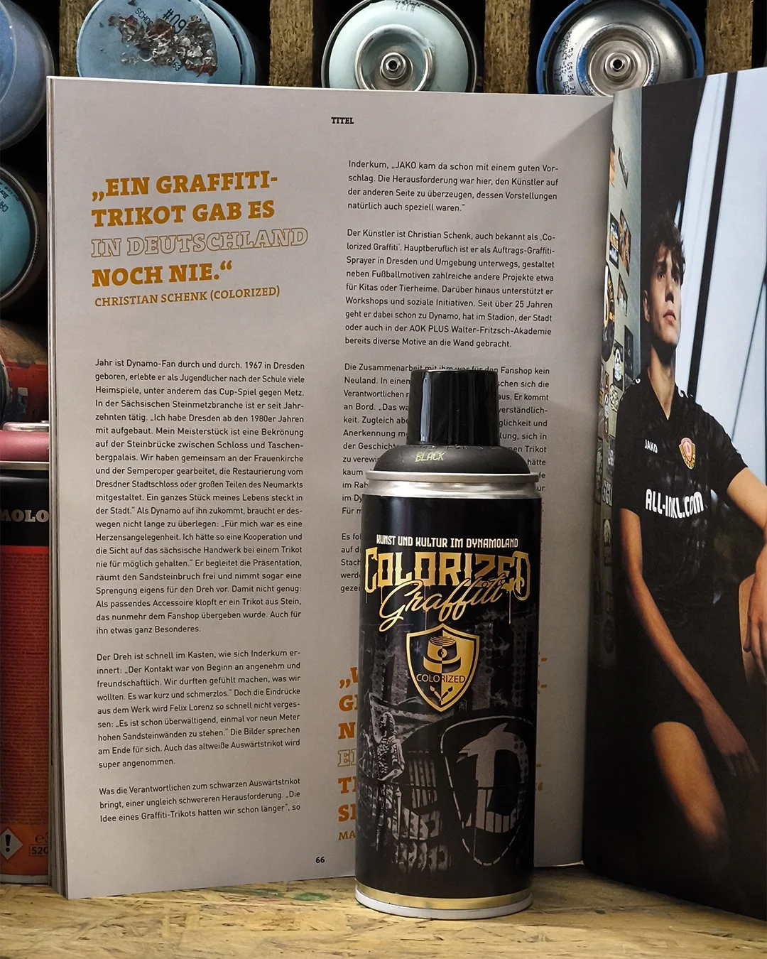 Auf diesem Bild sind mehrere Tresor- oder Geldbriefkassenschlösser an einer Holzplatte angebracht, die bemalt sind oder sich zum kreativen Graffiti-Sprayen eignen. Es liegt ein Informationsblatt in deutscher Sprache neben einem schwarzen Spraydosen-B