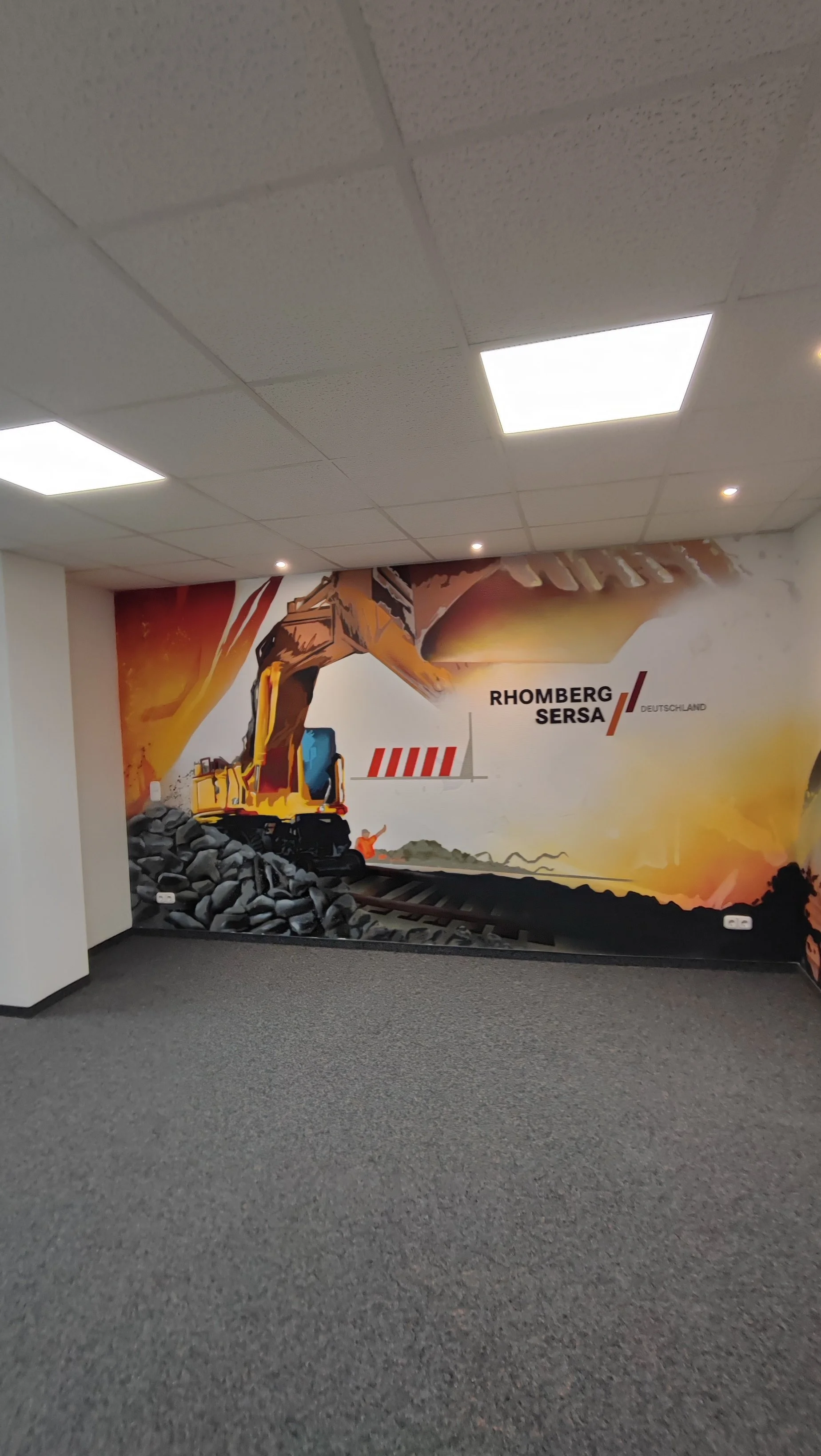 Wandbild eines Baufahrzeugs auf einer Baustelle in einer grauen Büro- oder Lagerhalle