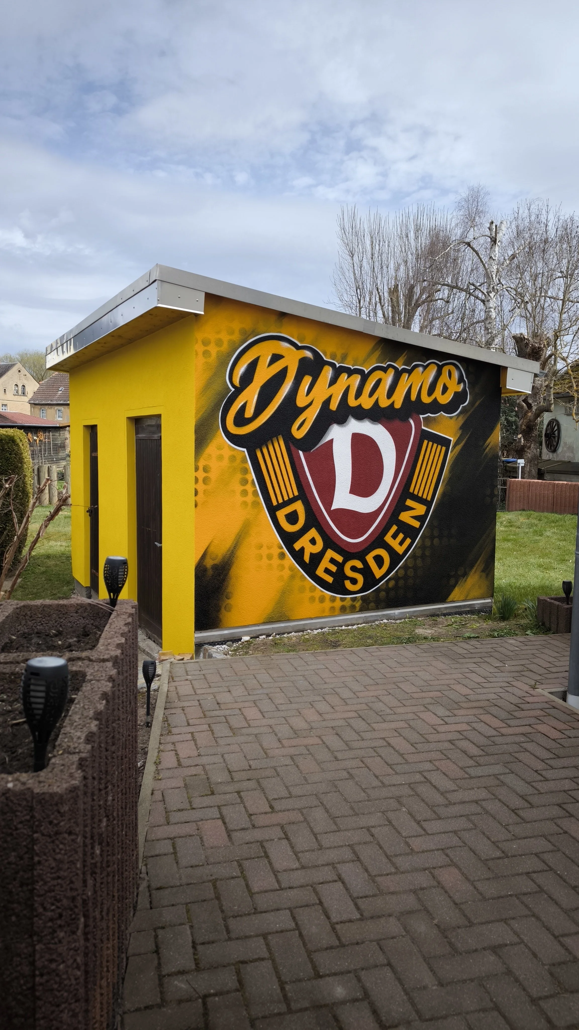 Klein gelbes Gebäude mit großem Dynamo-D Logo, das 'Dynamo Dresden' beschreibt, an der Außenseite.