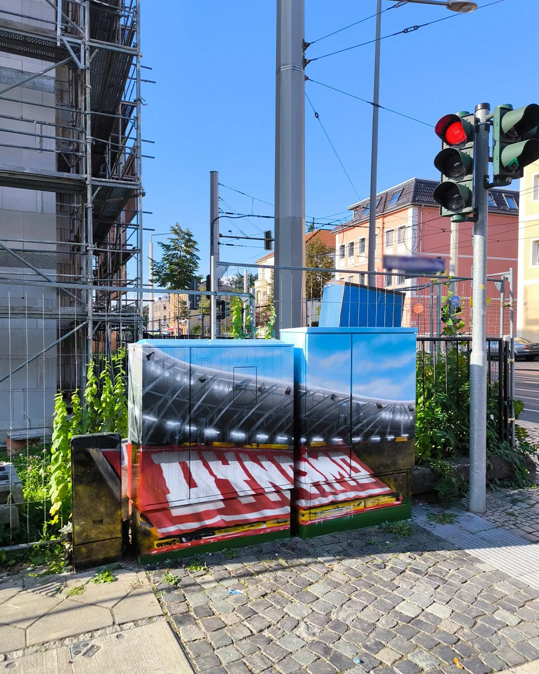 Kunstvolle Straßenlaterne, die wie ein großer, aufblasbarer Gegenstand aussieht. Es befindet sich an einer Straßenecke mit Verkehrsampel und Baugerüst im Hintergrund in einer städtischen Umgebung. Die Straßenlaterne ist reflektierend gestaltet und ha