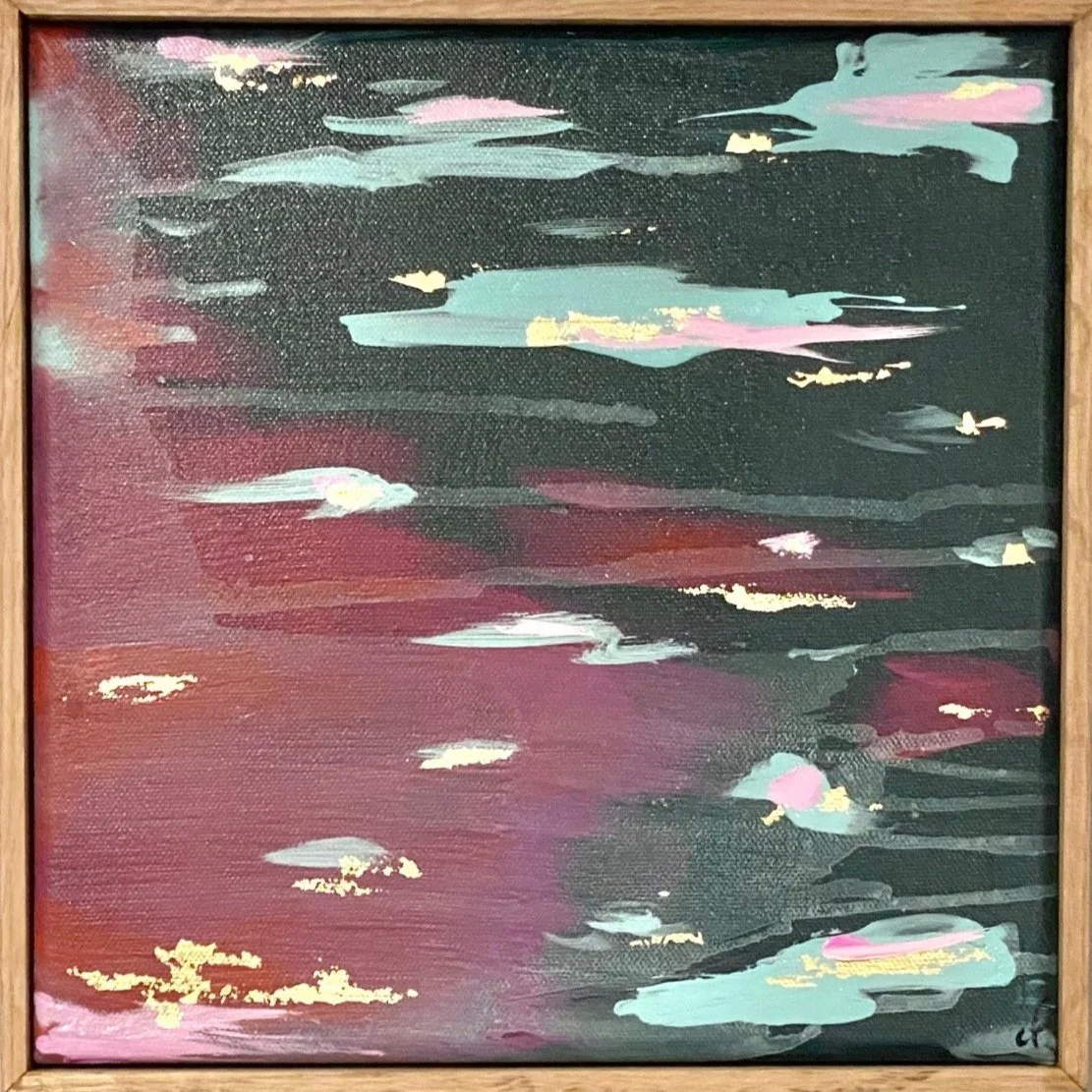 Abstract painting with dark background, splashes of pink, teal, and gold accents, framed in wood.