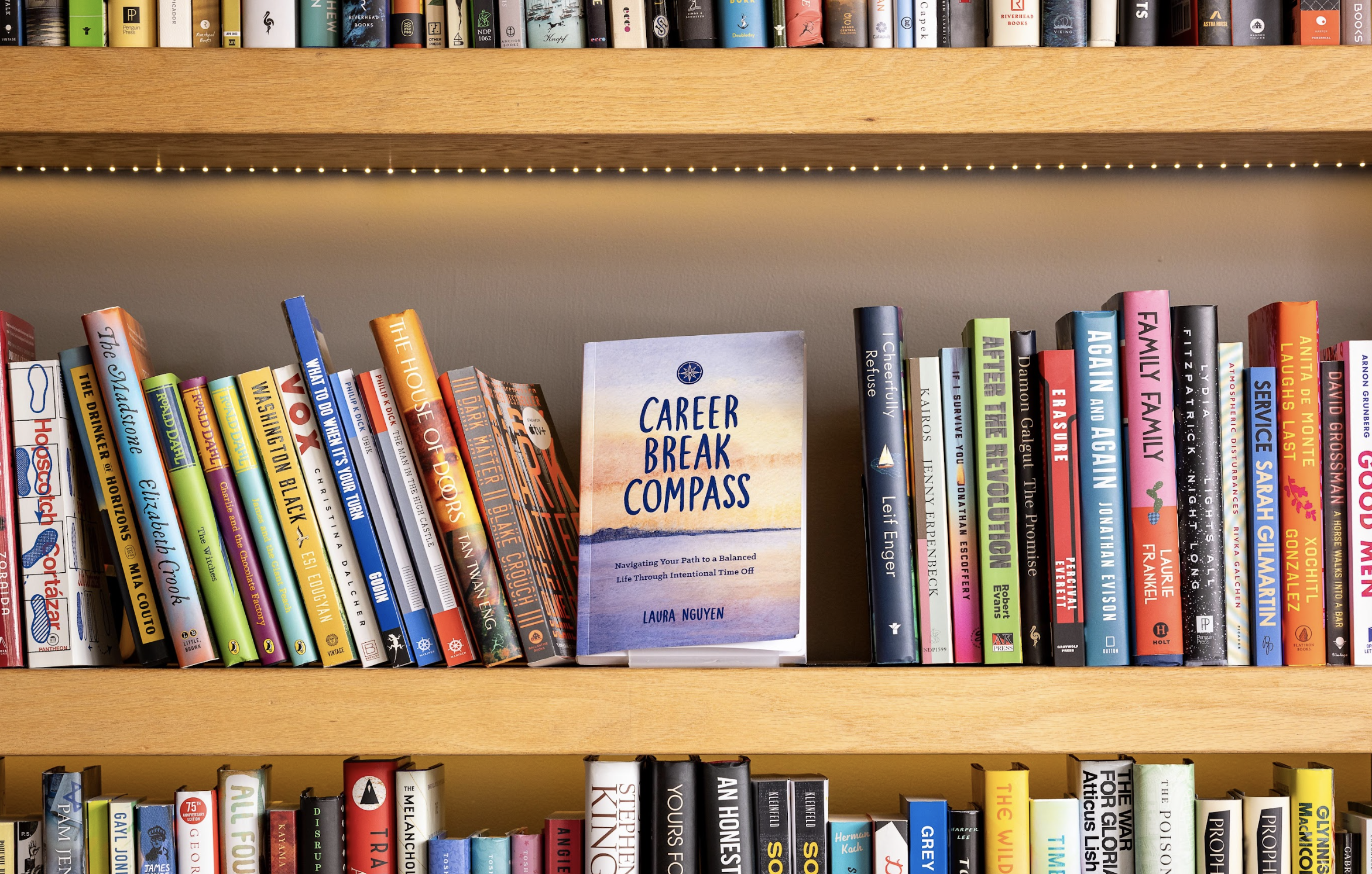 A bookshelf with a variety of books, including a prominent book titled 'Career Break Compass' by Laura Nguyen in the center, with colorful book covers on both sides.