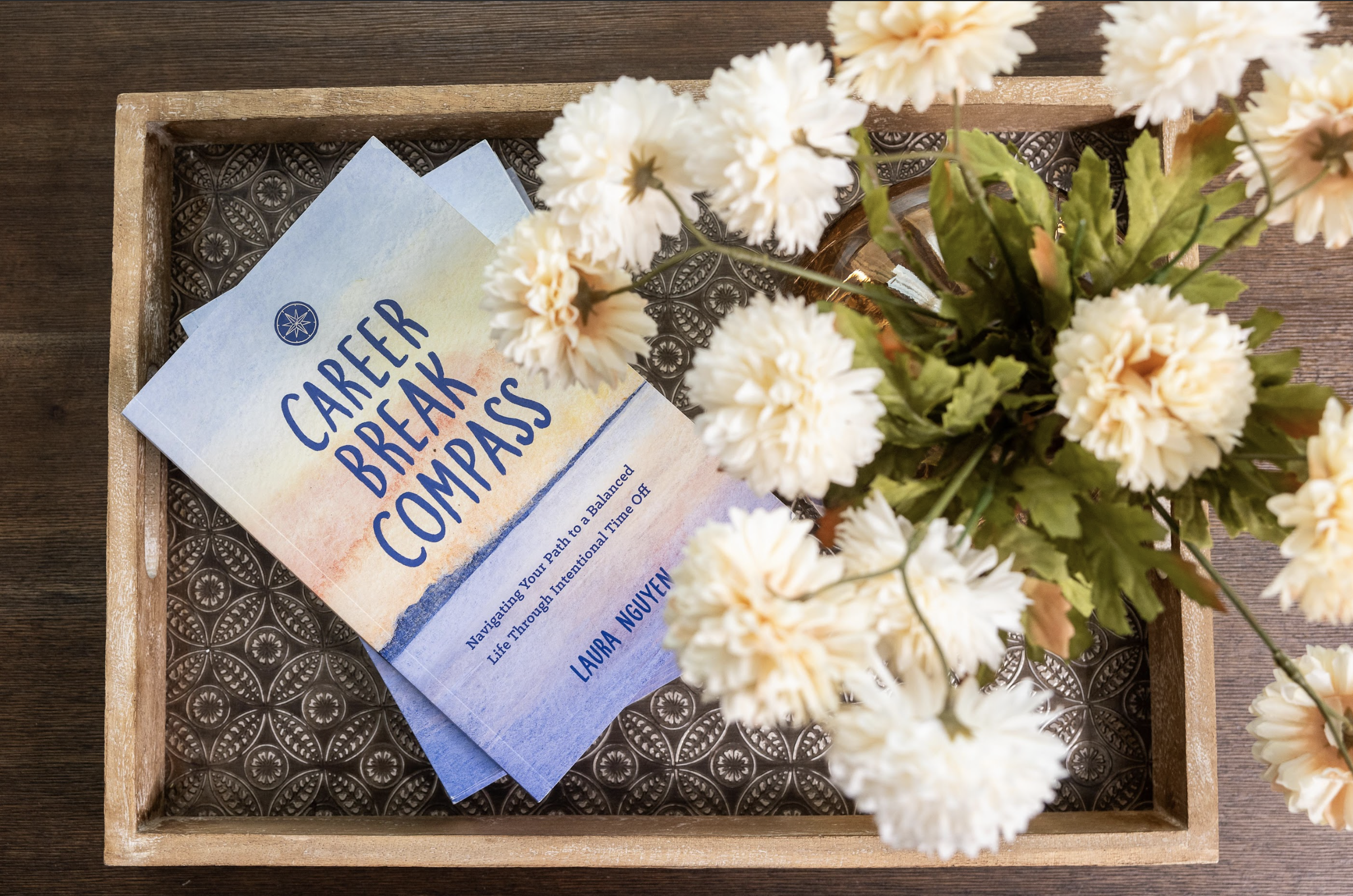 A wooden tray with a stack of comfort travel guides and a bouquet of white flowers.