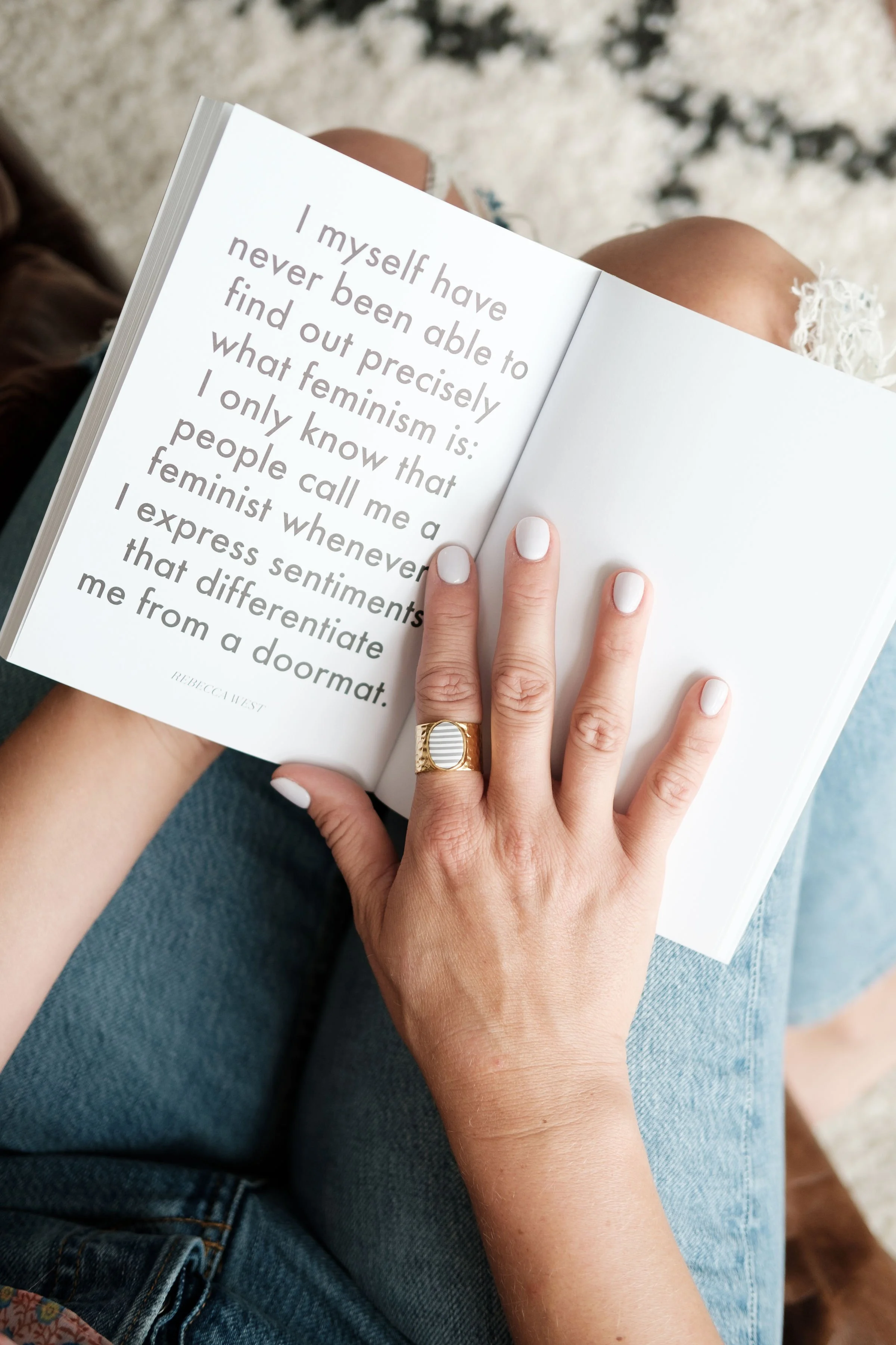 Person holding an open book with a quote that reads, "I myself have never been able to find out precisely what feminism is: I only know that people call me a feminist whenever I express sentiments that differentiate me from a doormat."