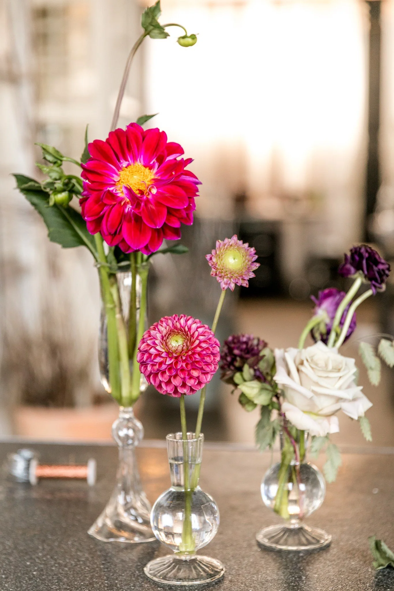 Various vibrant flowers in small glass vases on a dark countertop.