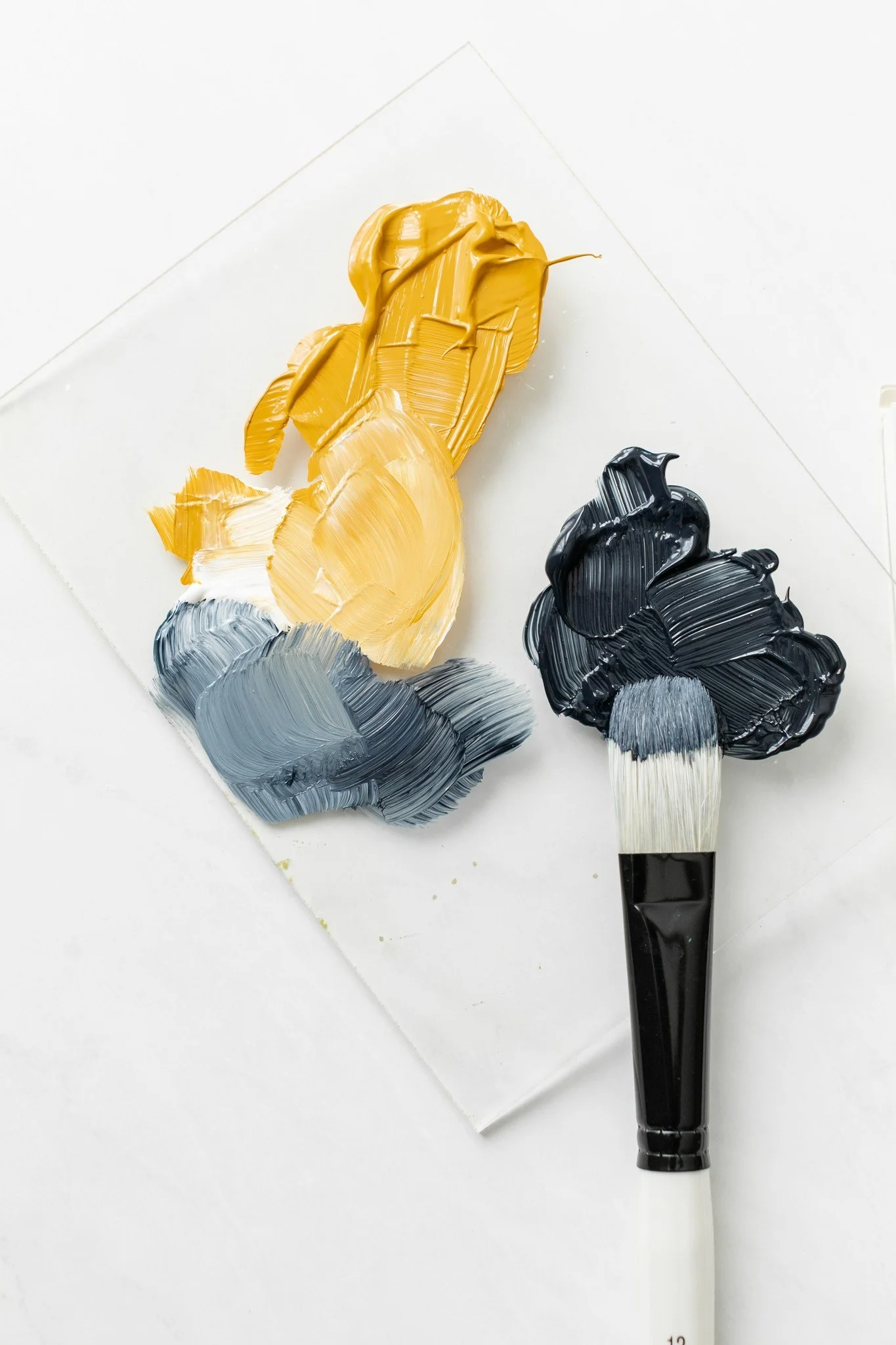 Paint palette with yellow, gray, and black paint, with a paintbrush covered in black and white paint resting on the palette.