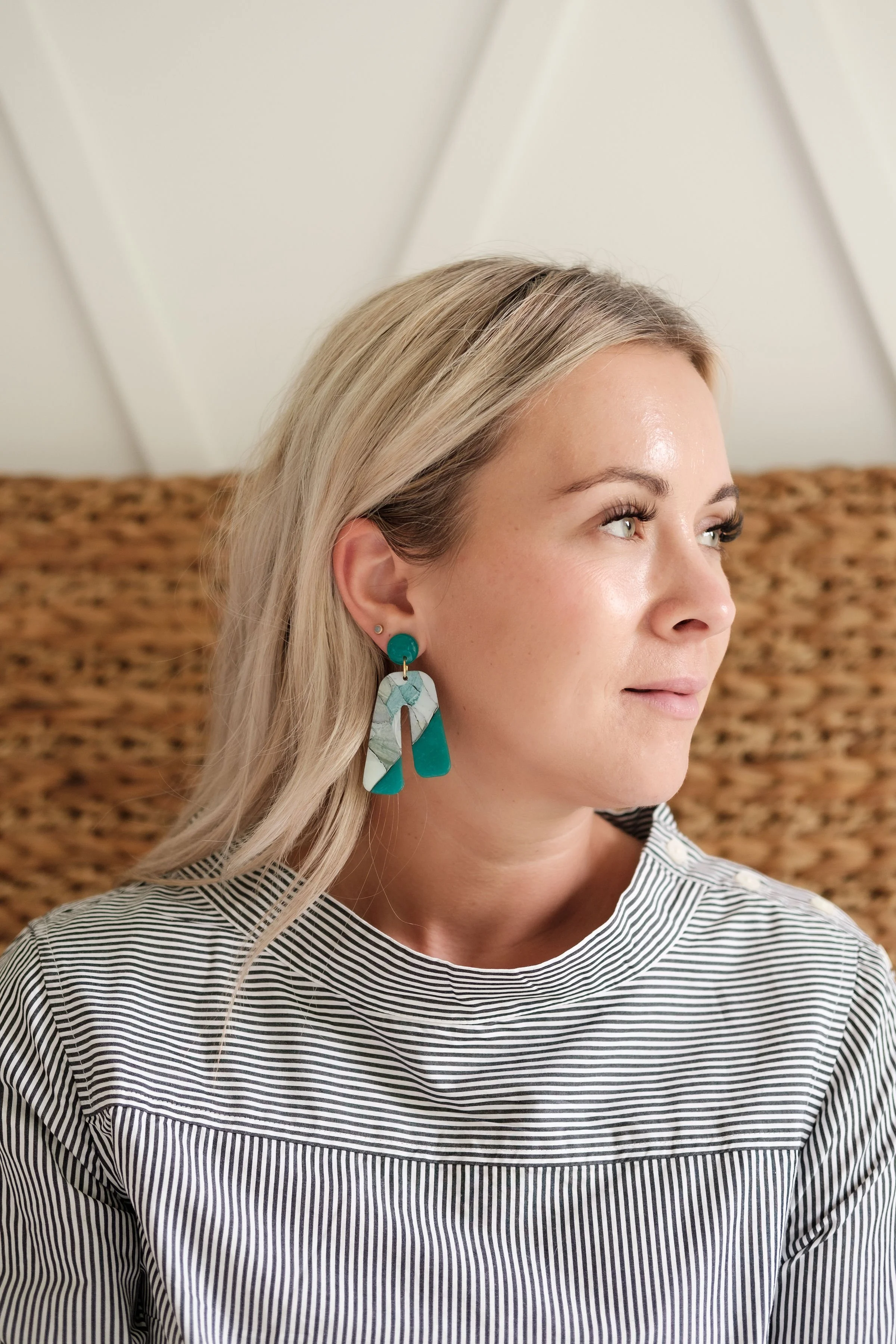A woman with blonde hair and earrings, wearing a black and white striped top, looking to the right.