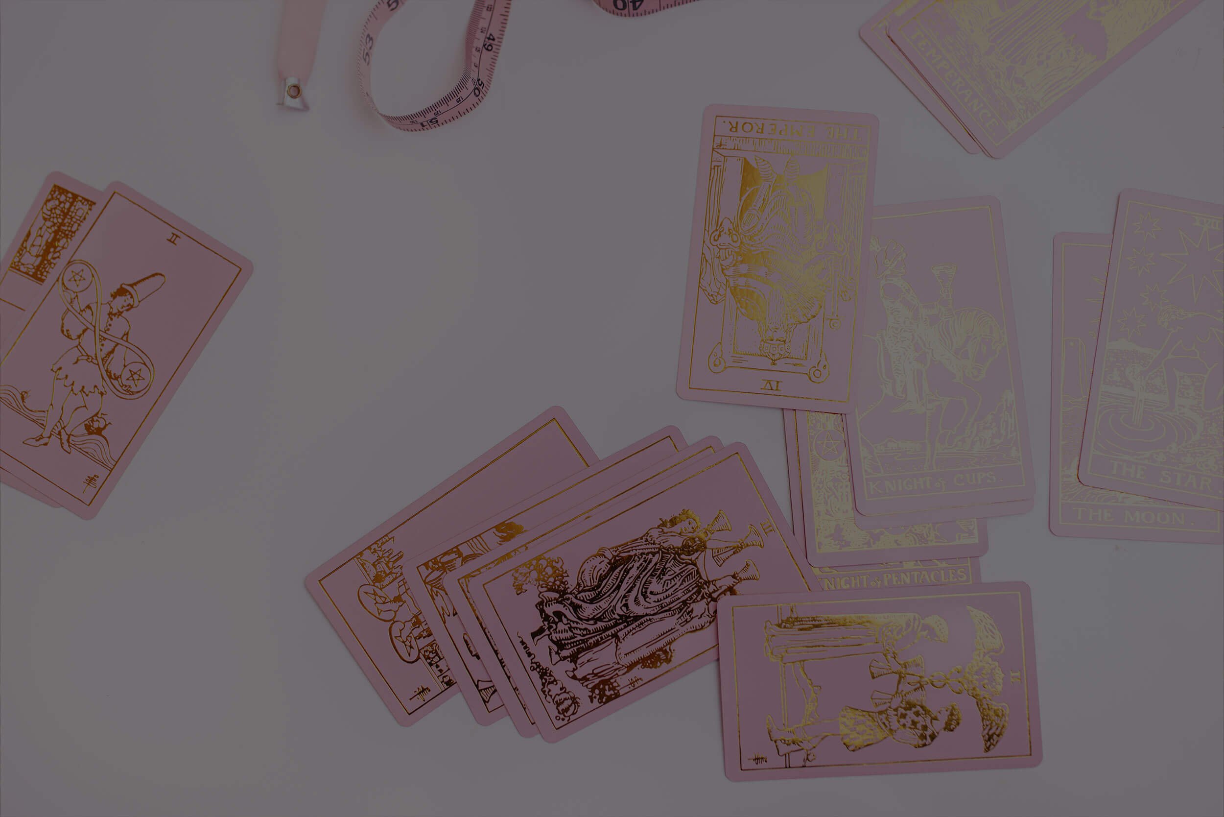 Tarot cards spread out on a white surface with a pink measuring tape nearby.