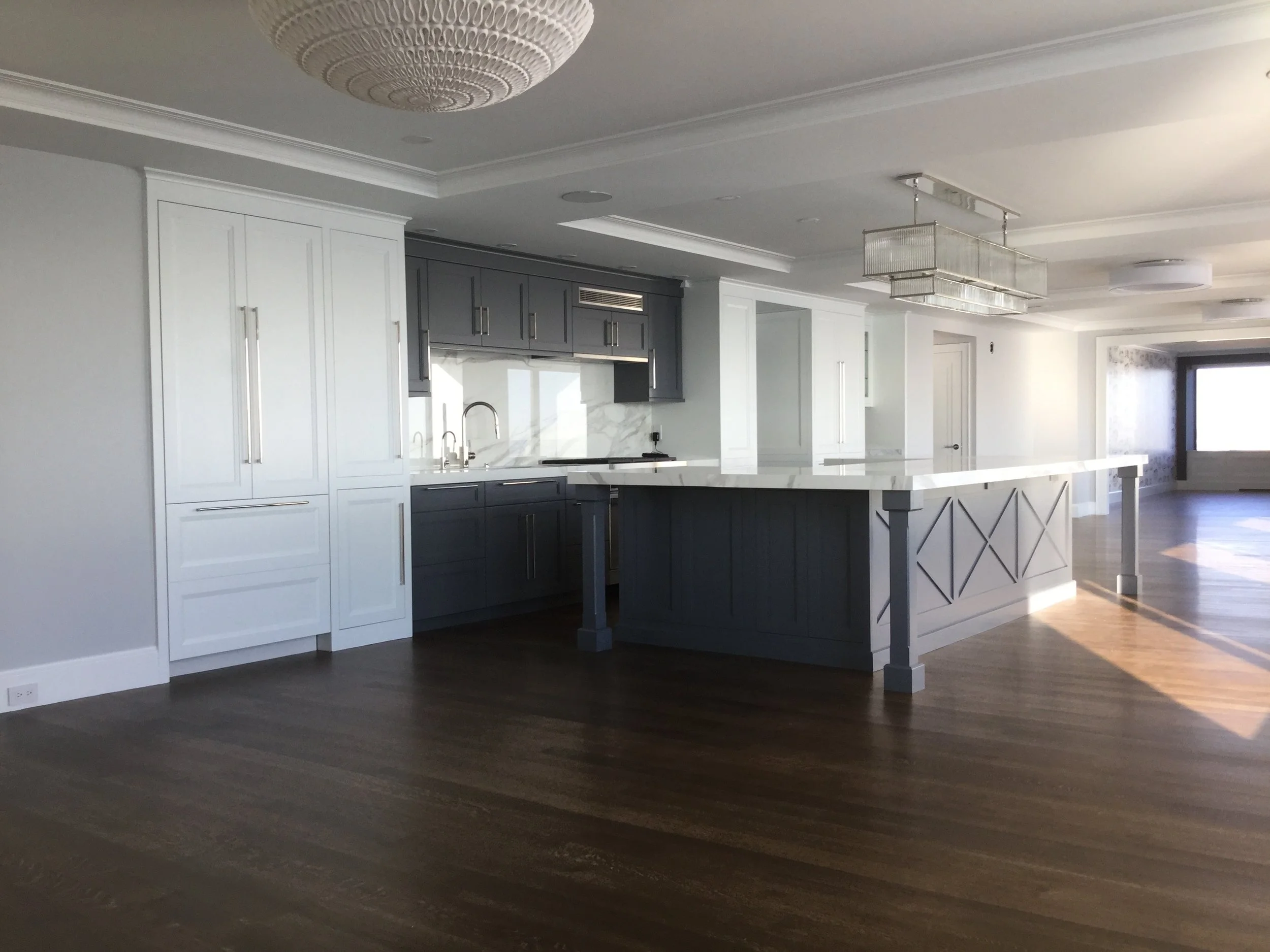 Modern kitchen with white and gray cabinetry, a large central island with a white countertop, and hardwood floors. There is a window bringing in natural light.