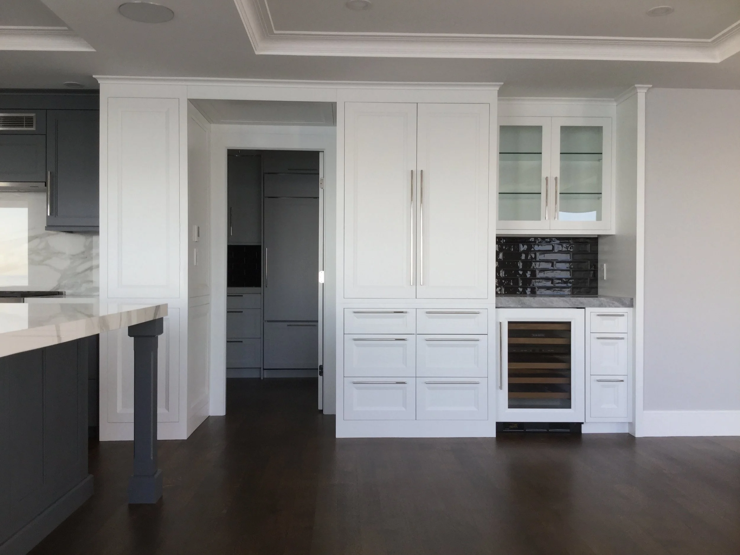 Modern kitchen with white cabinetry, black backsplash, and wine fridge, with a partial view of a gray island on the left.