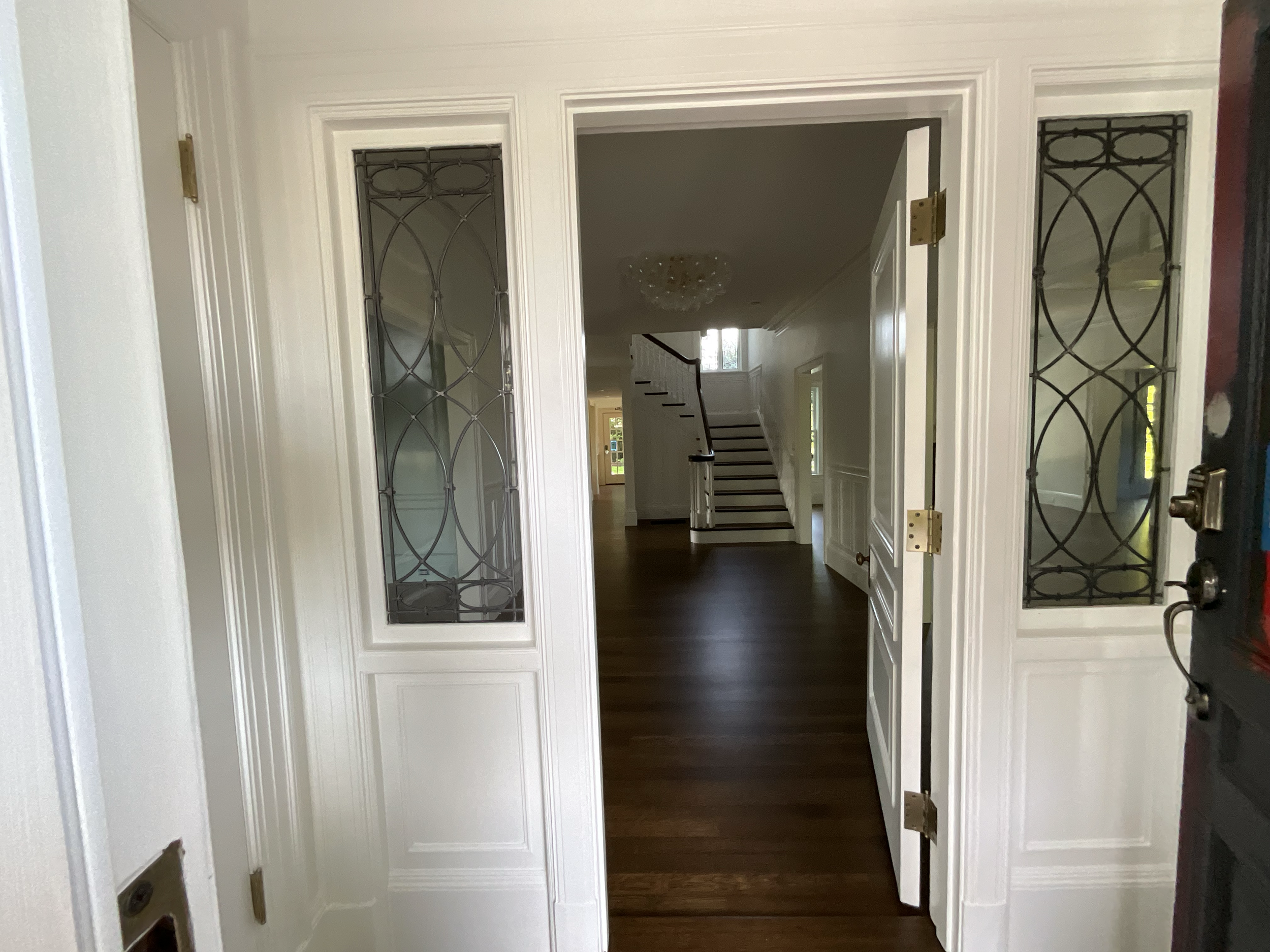 View of a home's interior entryway through double front doors with glass panels, looking into a living space with stairs, hardwood floors, and a chandelier.