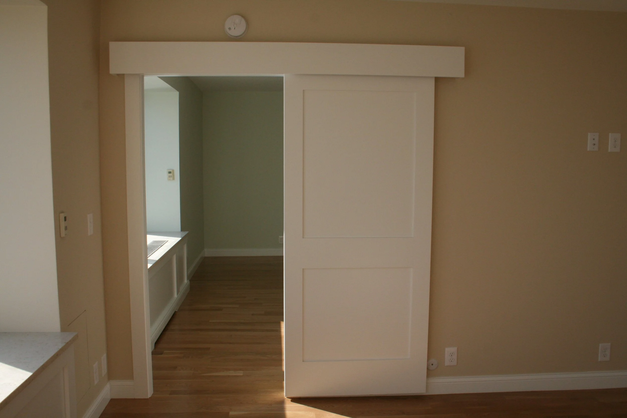 Empty room with beige walls, hardwood floors, a sliding door, and multiple electrical outlets.