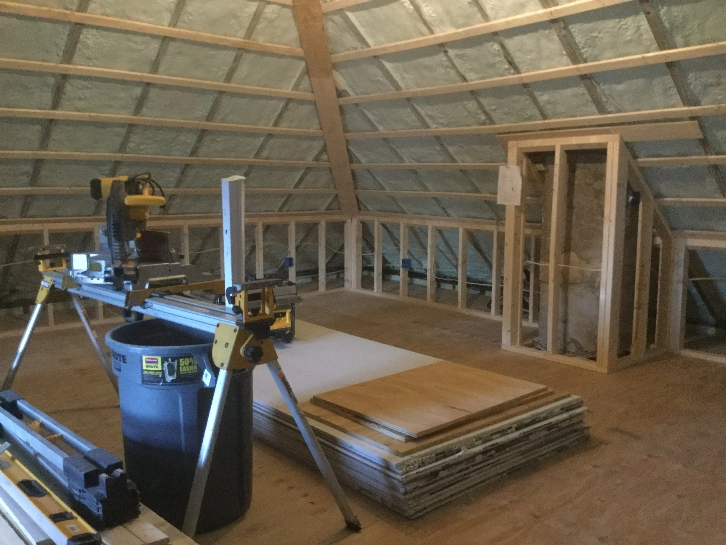 Interior attic under construction with framing, plywood, tools, and building supplies stored around.