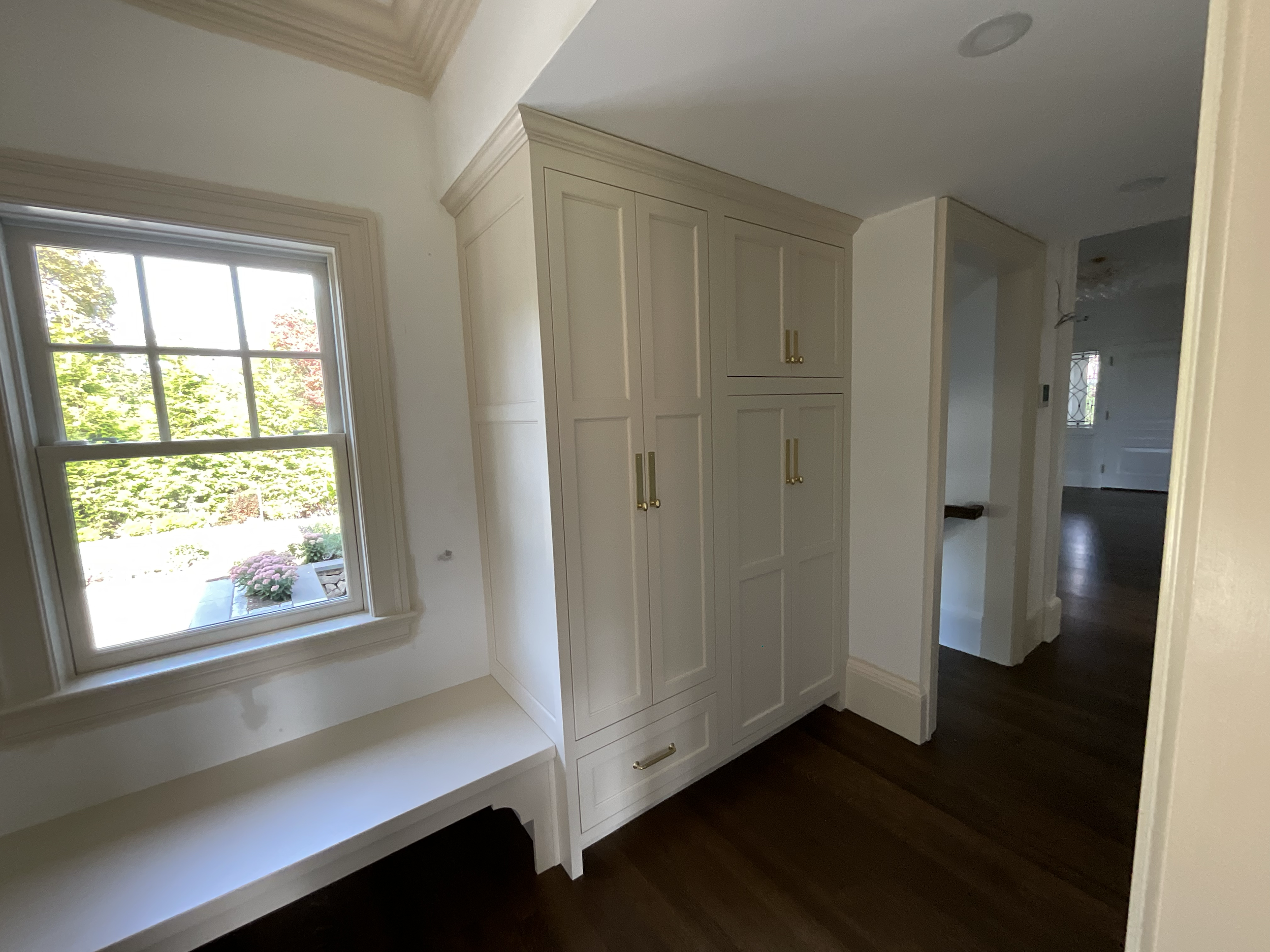 Interior view of a home with a window, a built-in white cabinet with gold handles, and dark hardwood floors.
