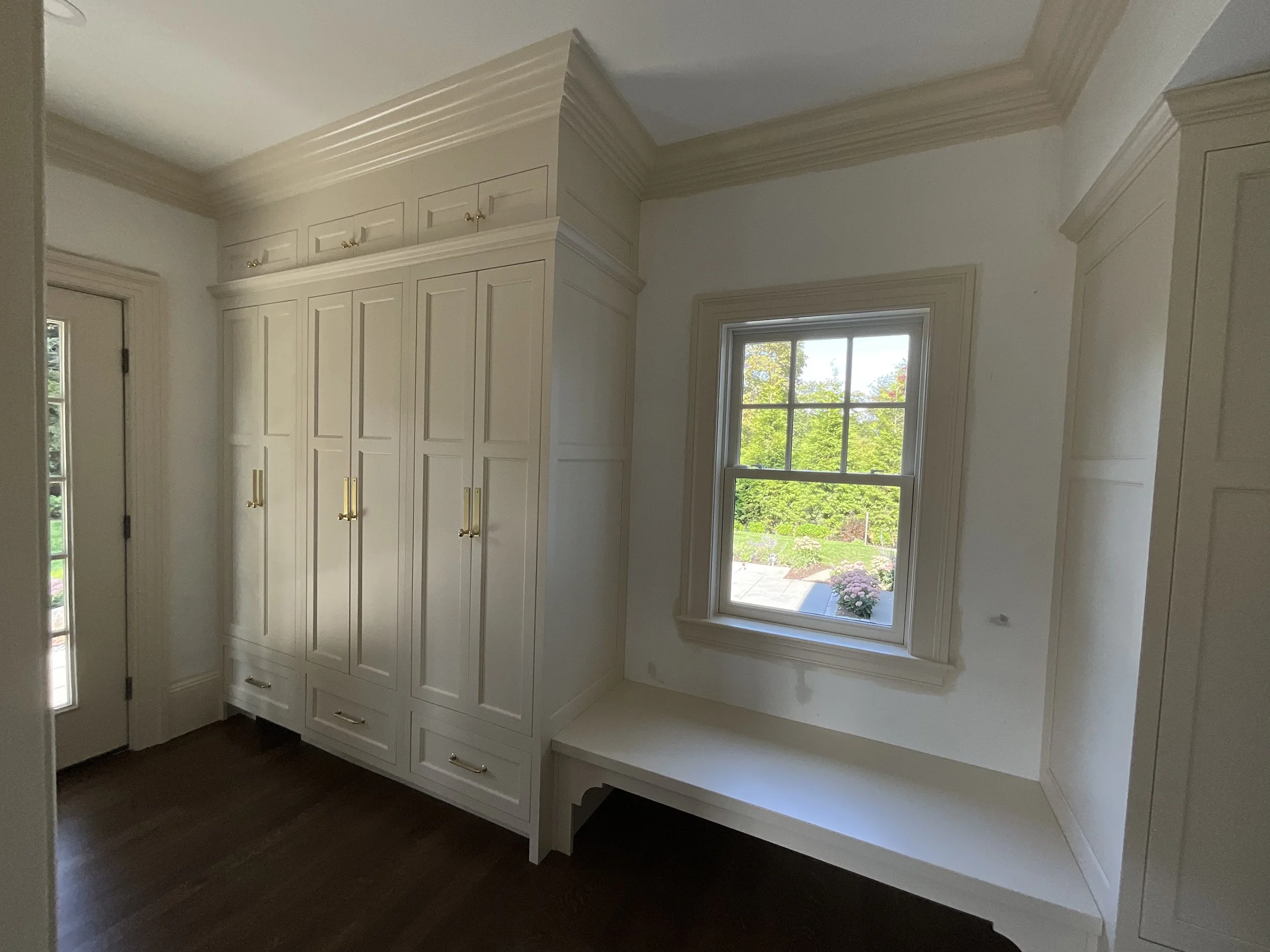Interior of a room with beige built-in cabinets, a window with a garden view, and a dark wooden floor.