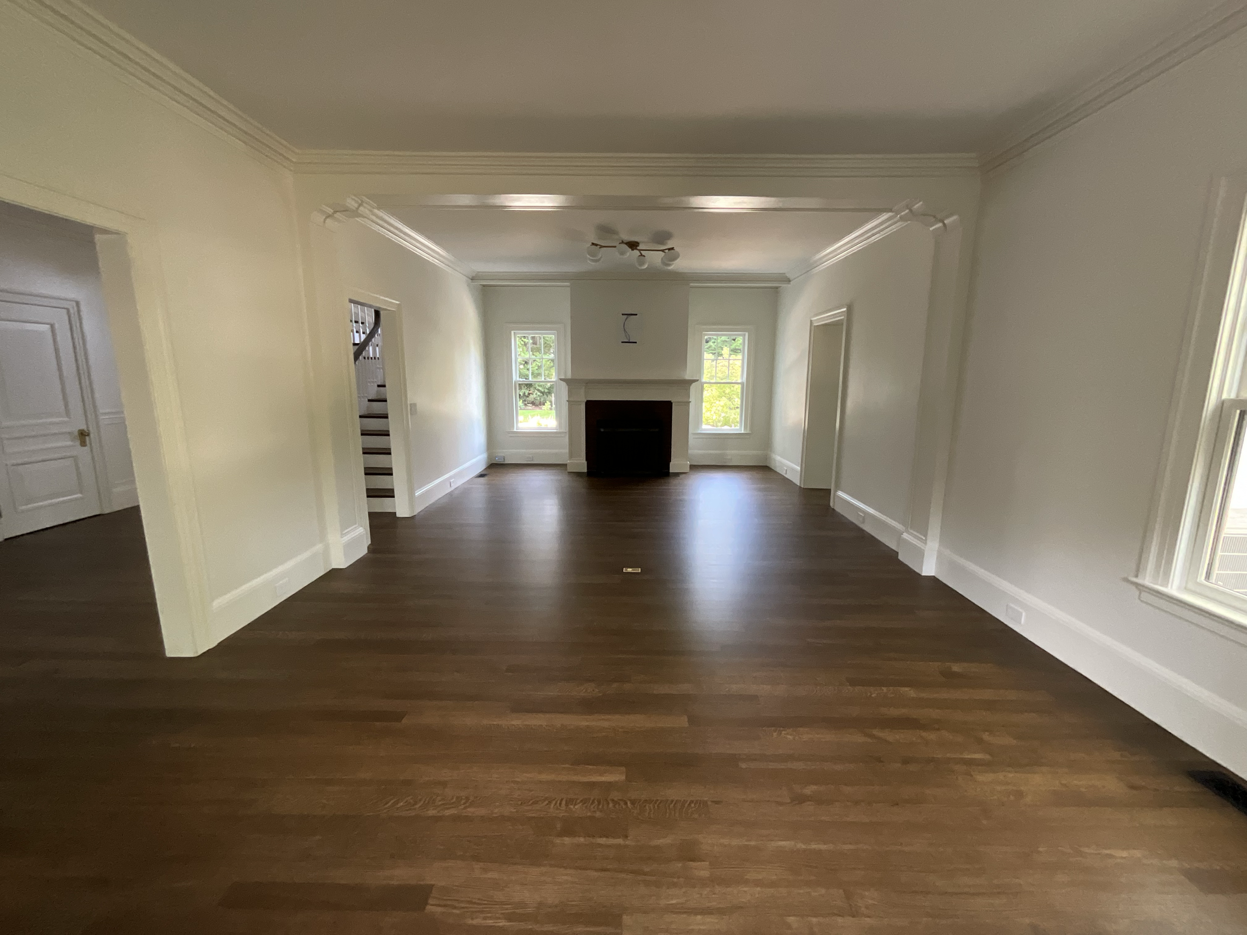 Empty living room with white walls, hardwood flooring, a fireplace between two windows, and crown molding.