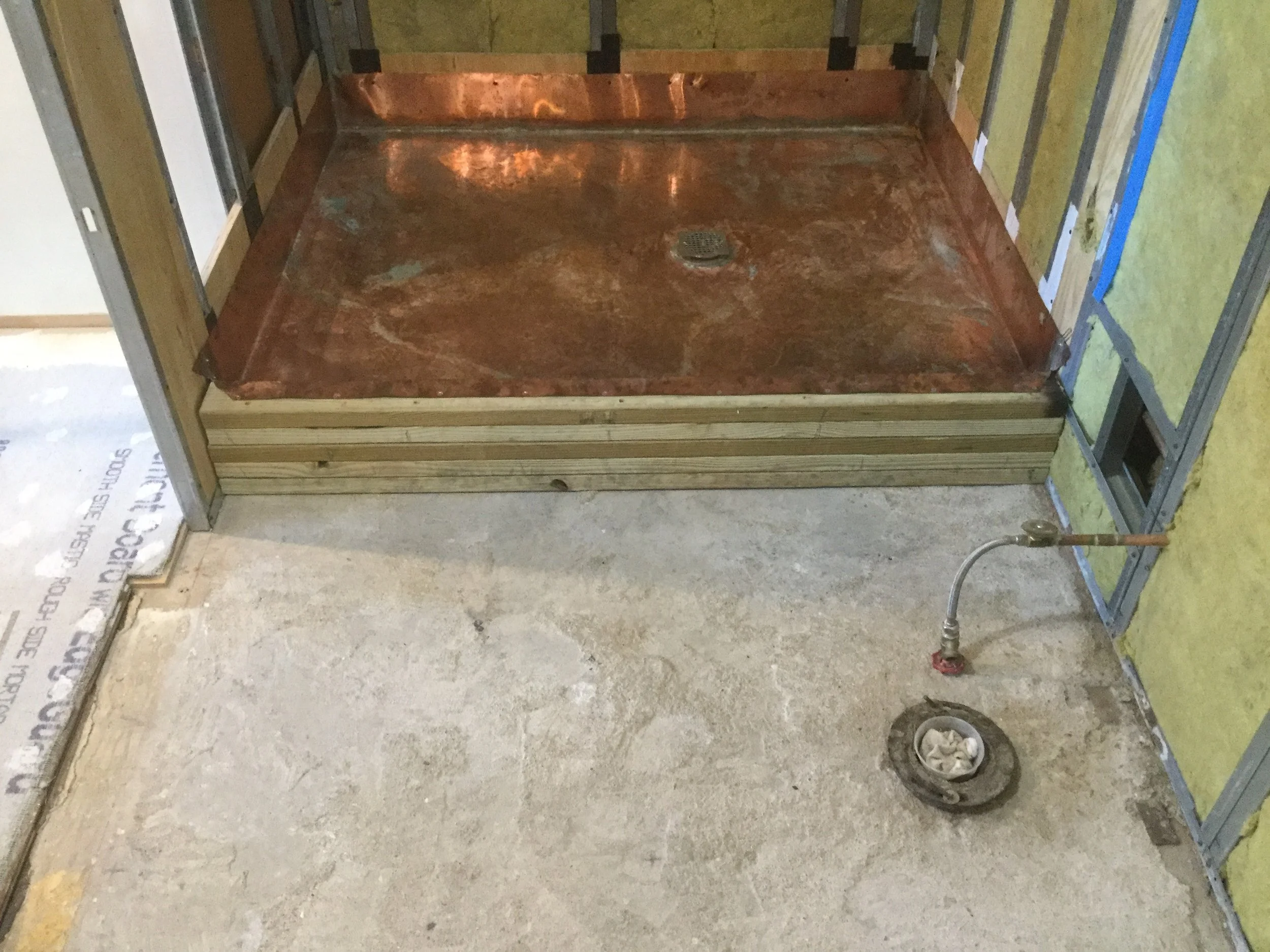 Shower area in construction with copper shower pan, unfinished wall framing, and plumbing in place.