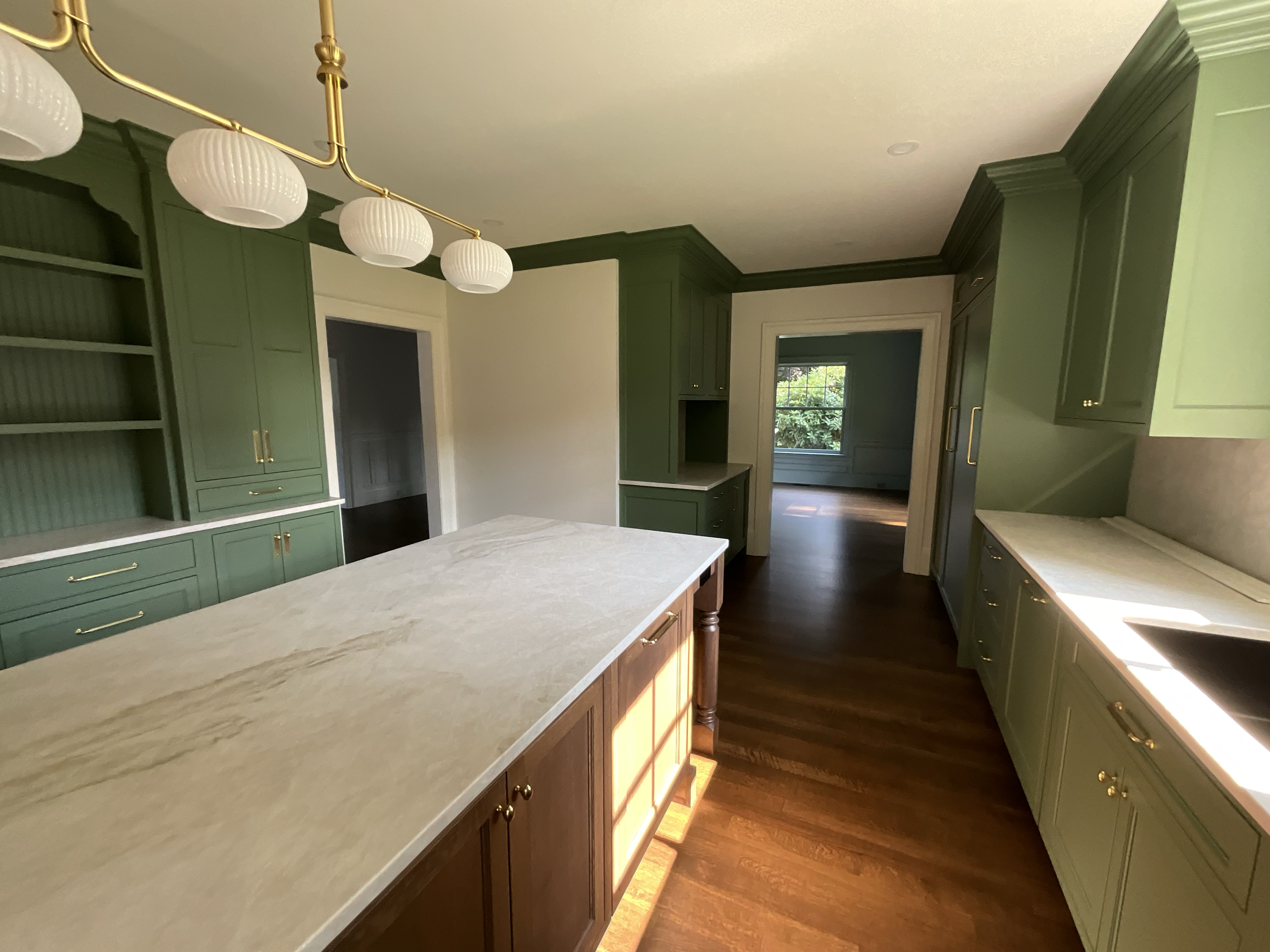 A kitchen with green cabinetry, a white marble countertop island, and a hanging light fixture with five white spherical lamps.