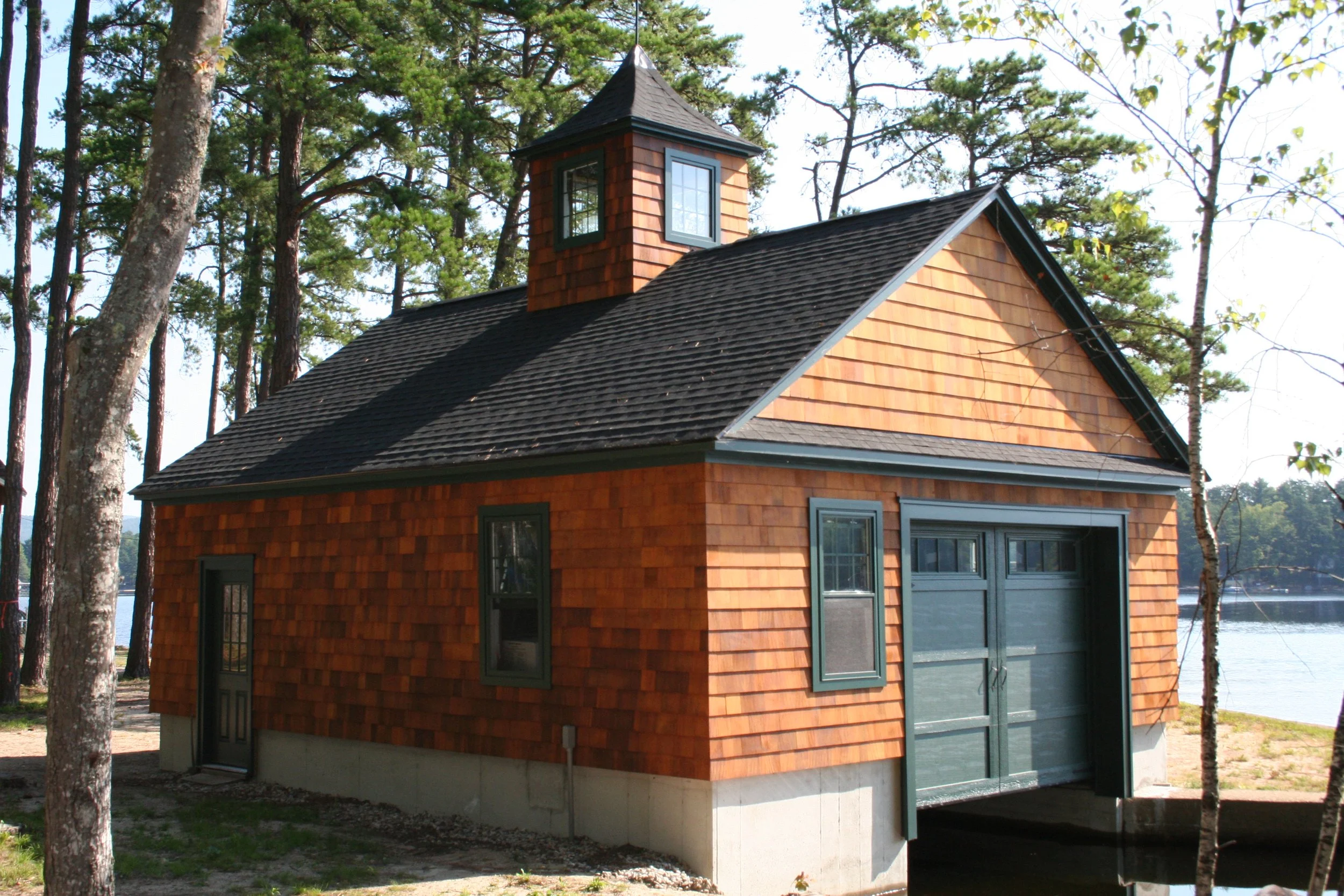 A small wooden building with a garage door, set among trees near a body of water.