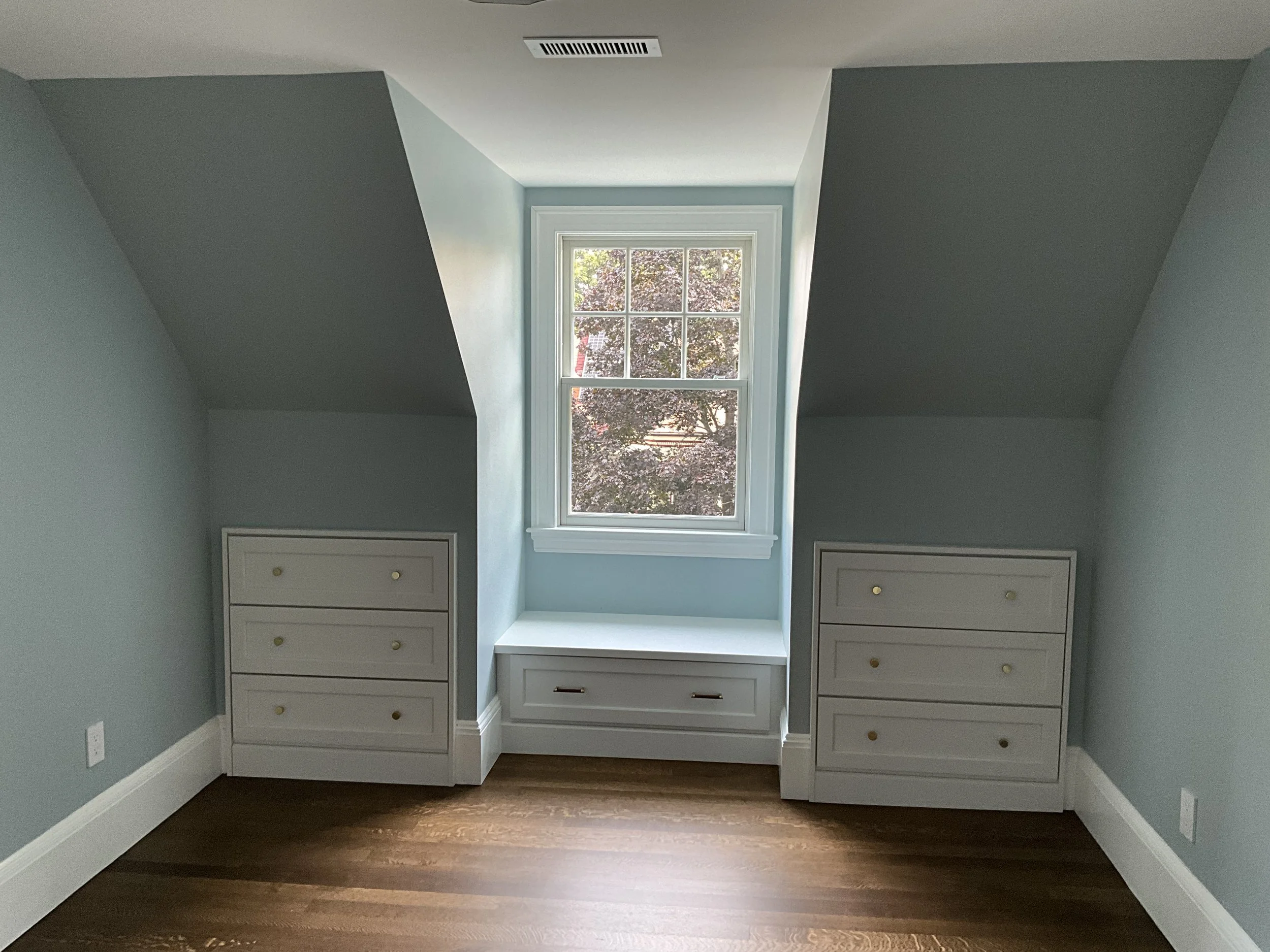 Small room with a window above built-in storage benches with drawers on each side, light blue walls, white trim, hardwood floor, and ceiling vent.
