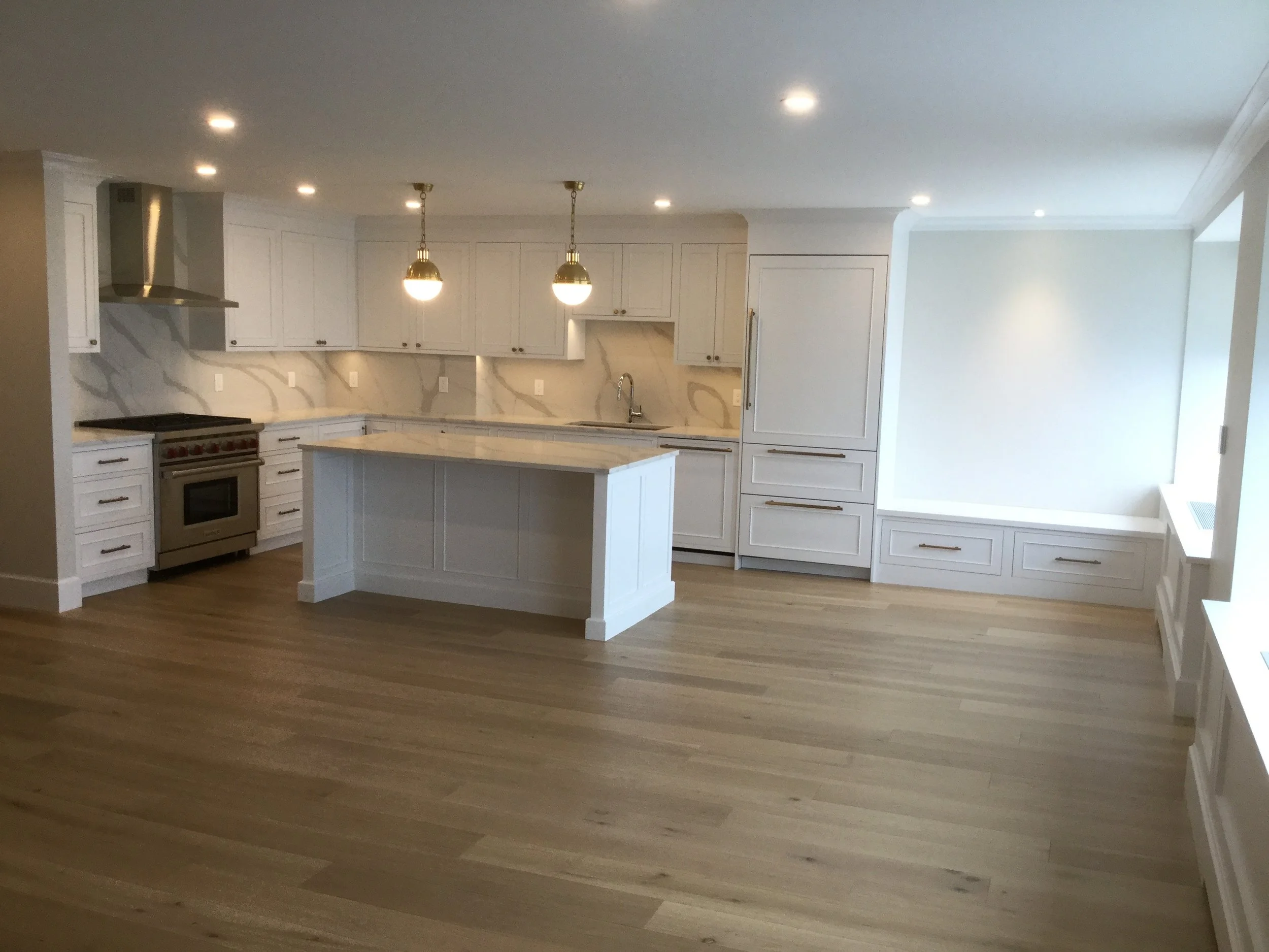 Modern kitchen with white cabinetry, marble countertops, a kitchen island, stainless steel oven, and hardwood flooring.