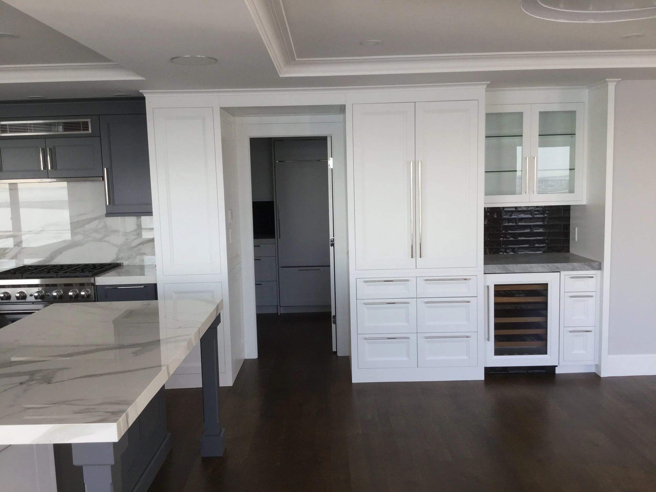 Modern kitchen with gray cabinets, a marble countertop, and a wine fridge. There is a doorway leading to another room.