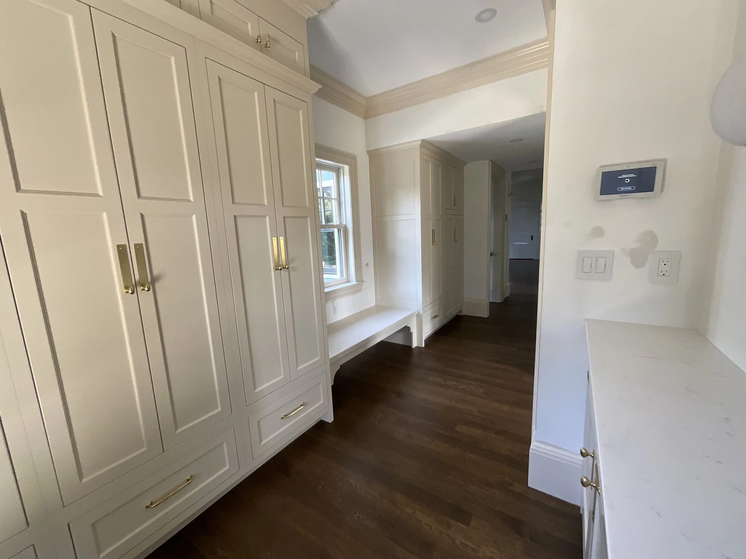 A room with white built-in cabinets and drawers, a window, and hardwood flooring.