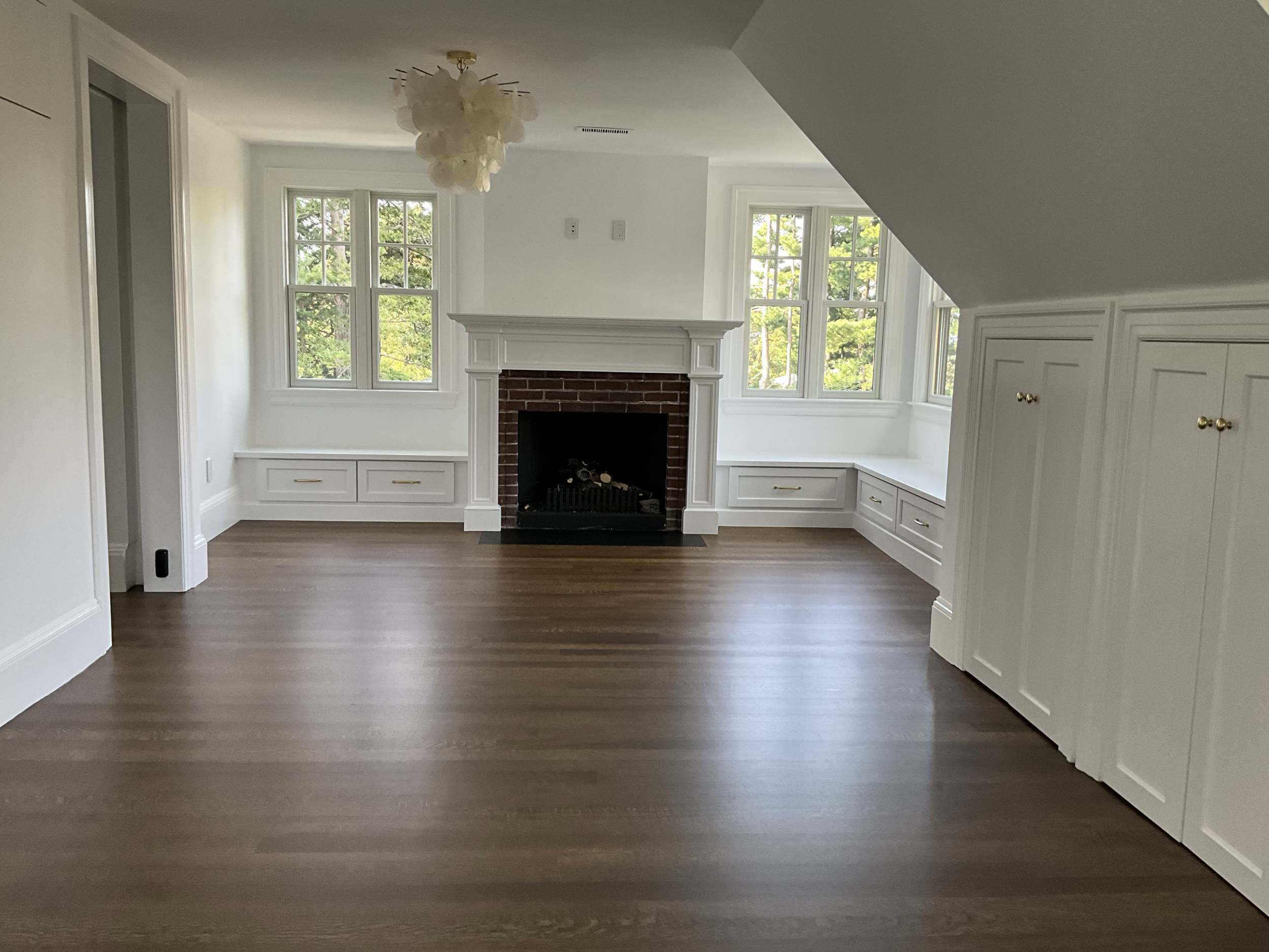 Empty room with hardwood floors, a fireplace, built-in white cabinets with gold knobs, and large windows letting in natural light.