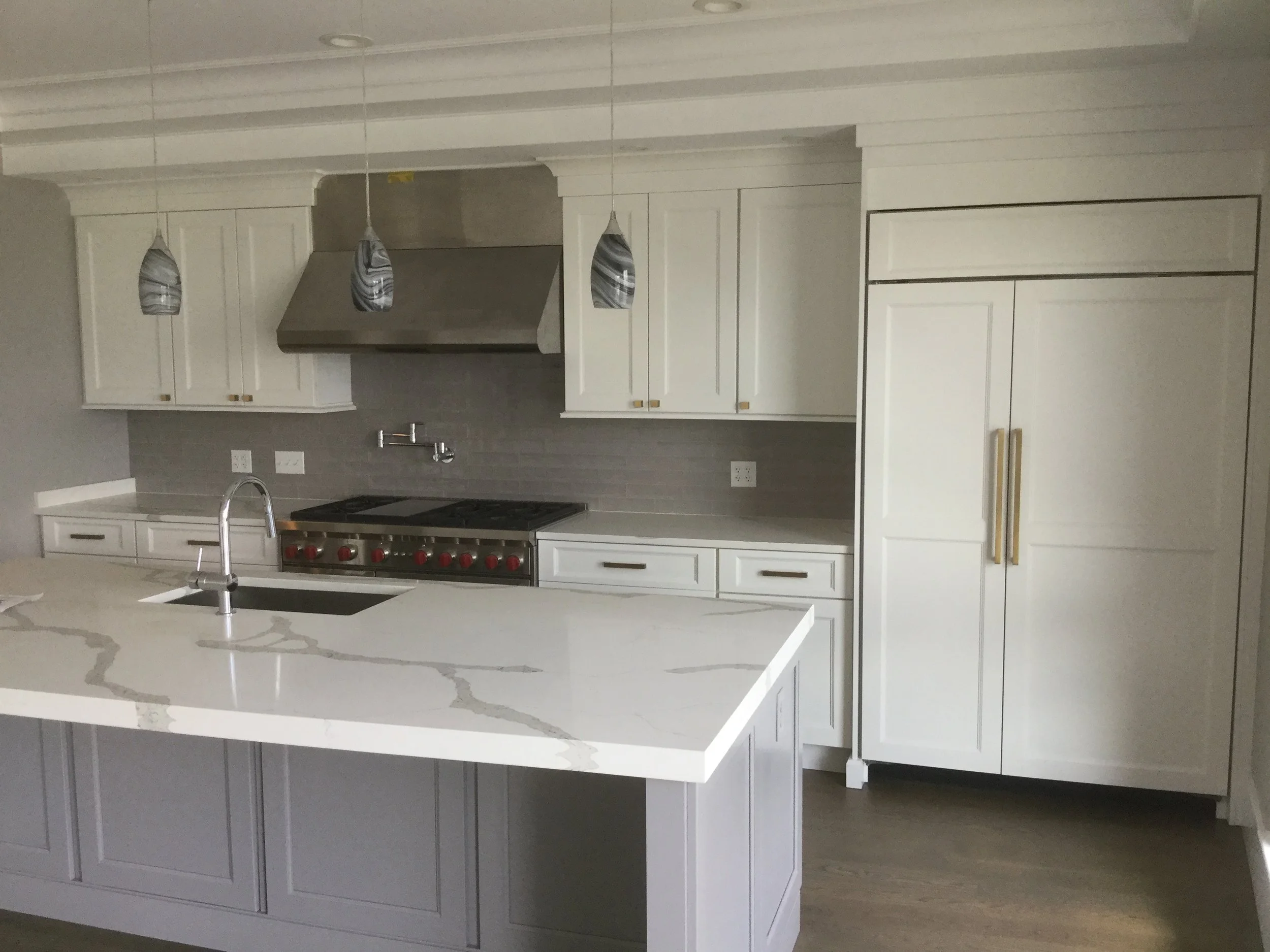 Modern kitchen with white cabinetry, a marble island with gray veining, stainless steel appliances, a gray subway tile backsplash, and three pendant lights.