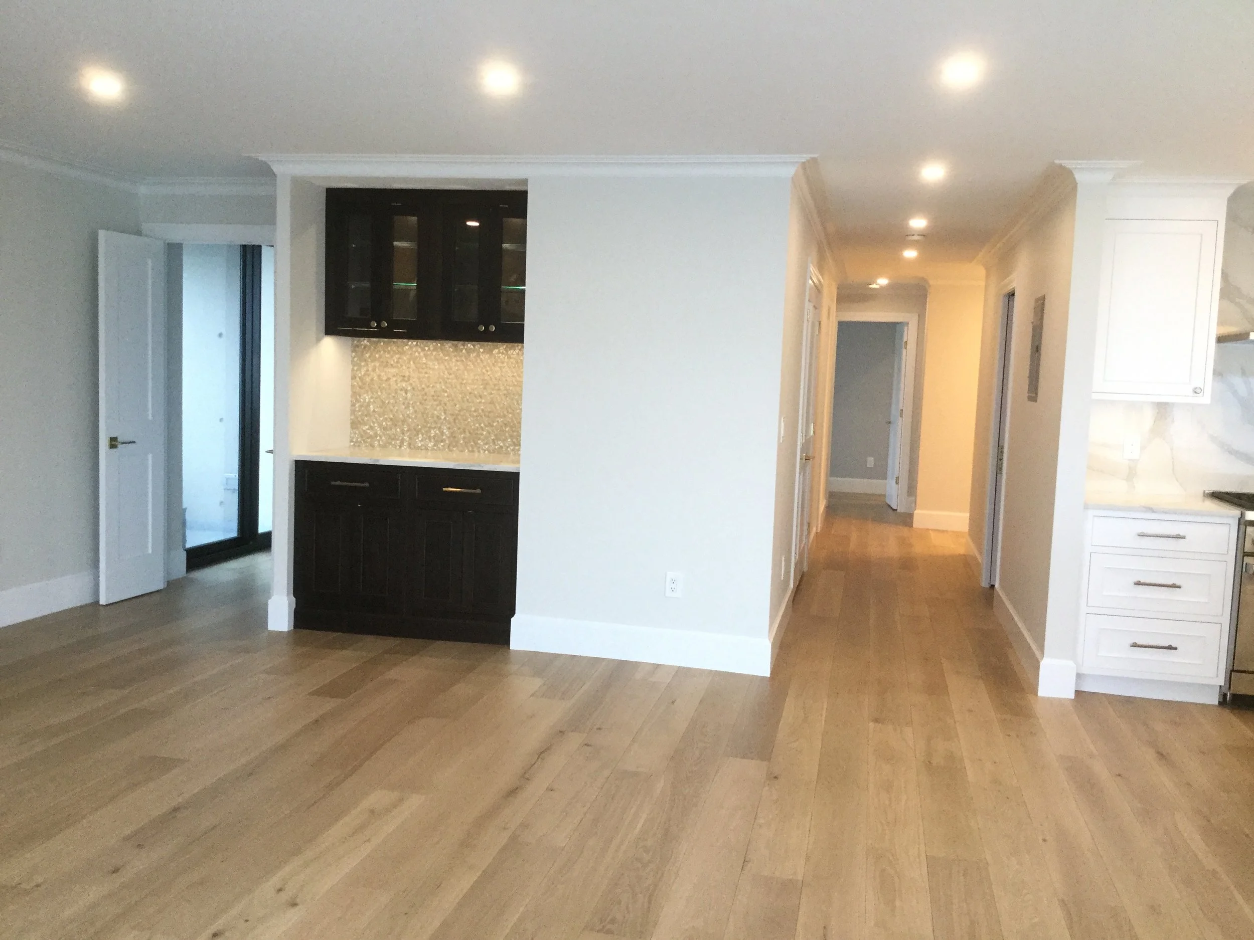 Empty modern kitchen with white and black cabinetry, hardwood floors, and recessed lighting.