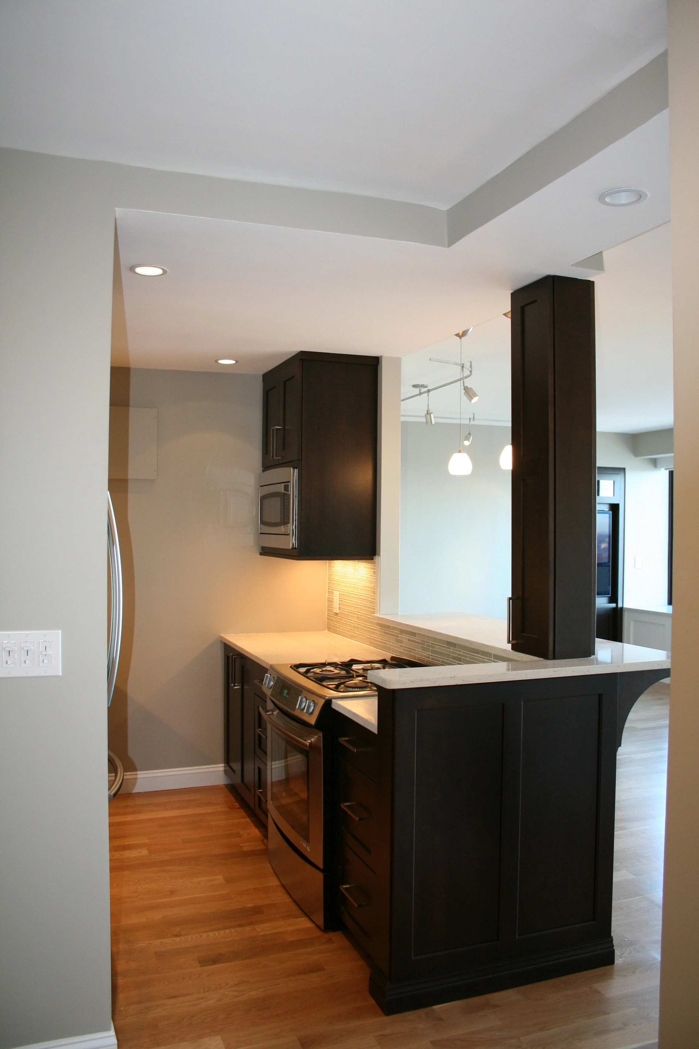 Modern kitchen with black cabinets, stainless steel appliances, a gas stove, and hardwood flooring.