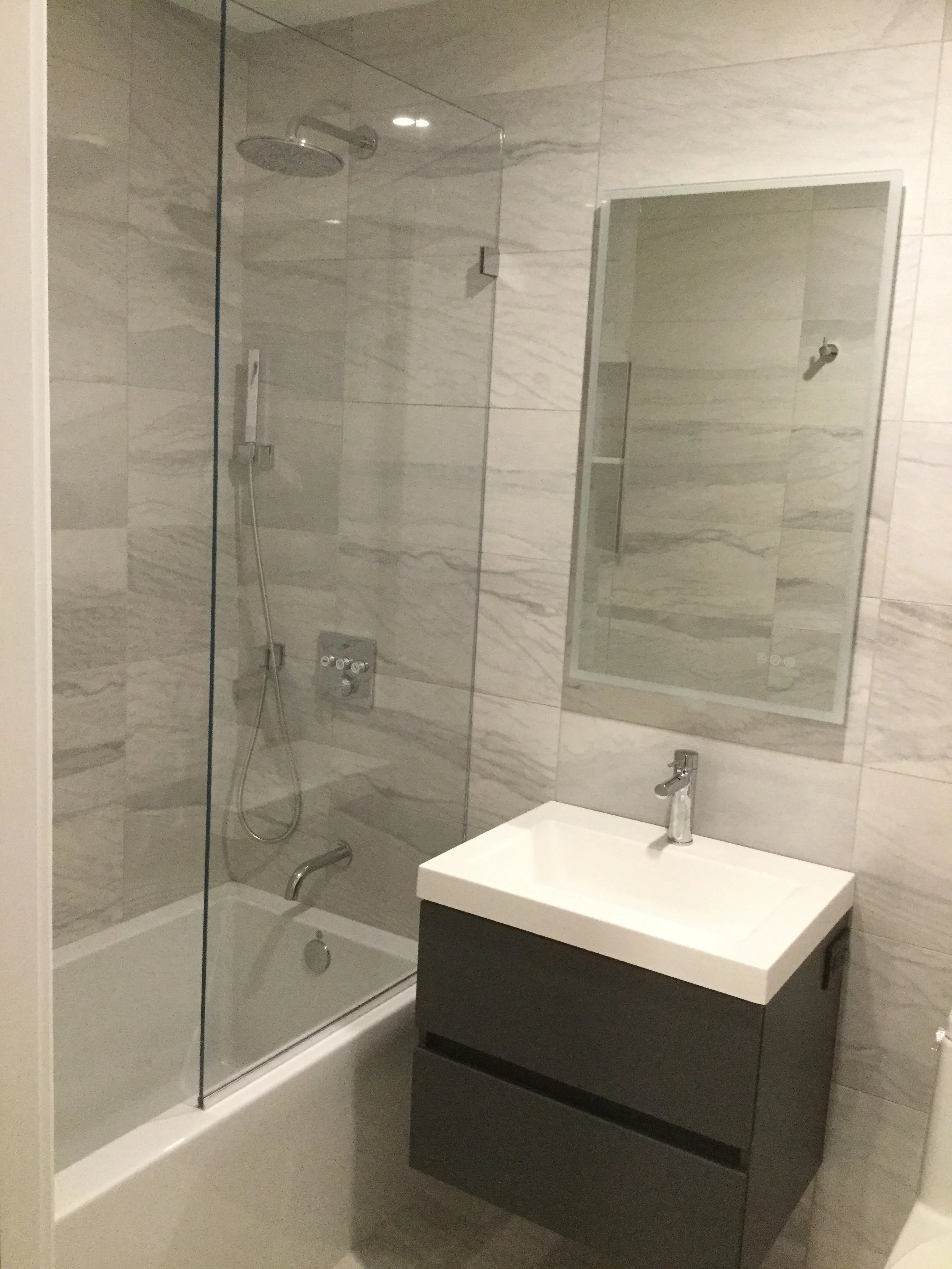 Modern bathroom with a glass-enclosed shower, a rectangular mirror, and a white sink with a black cabinet.