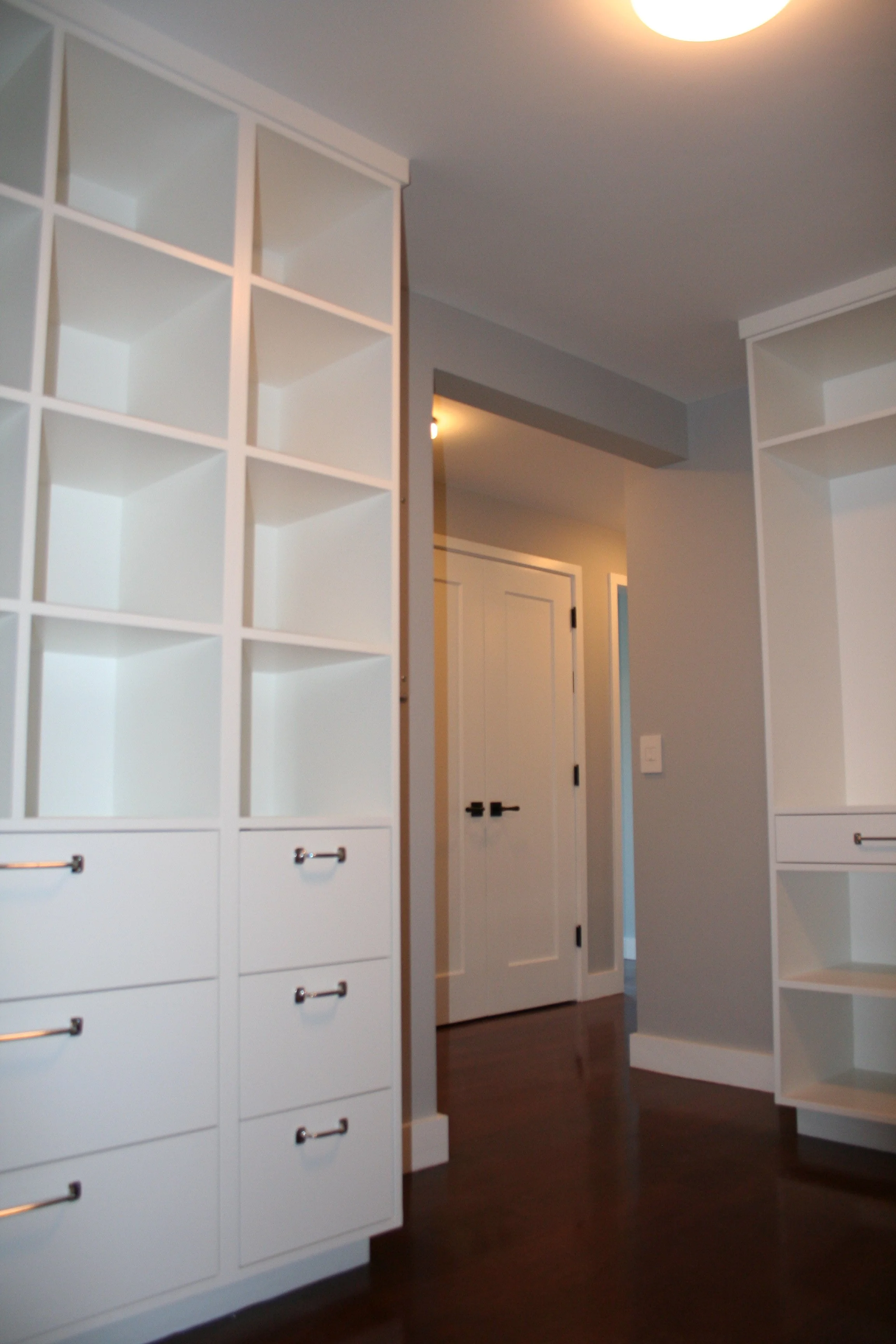 Empty white built-in shelves and drawers in a modern room with a doorway and hardwood floor.