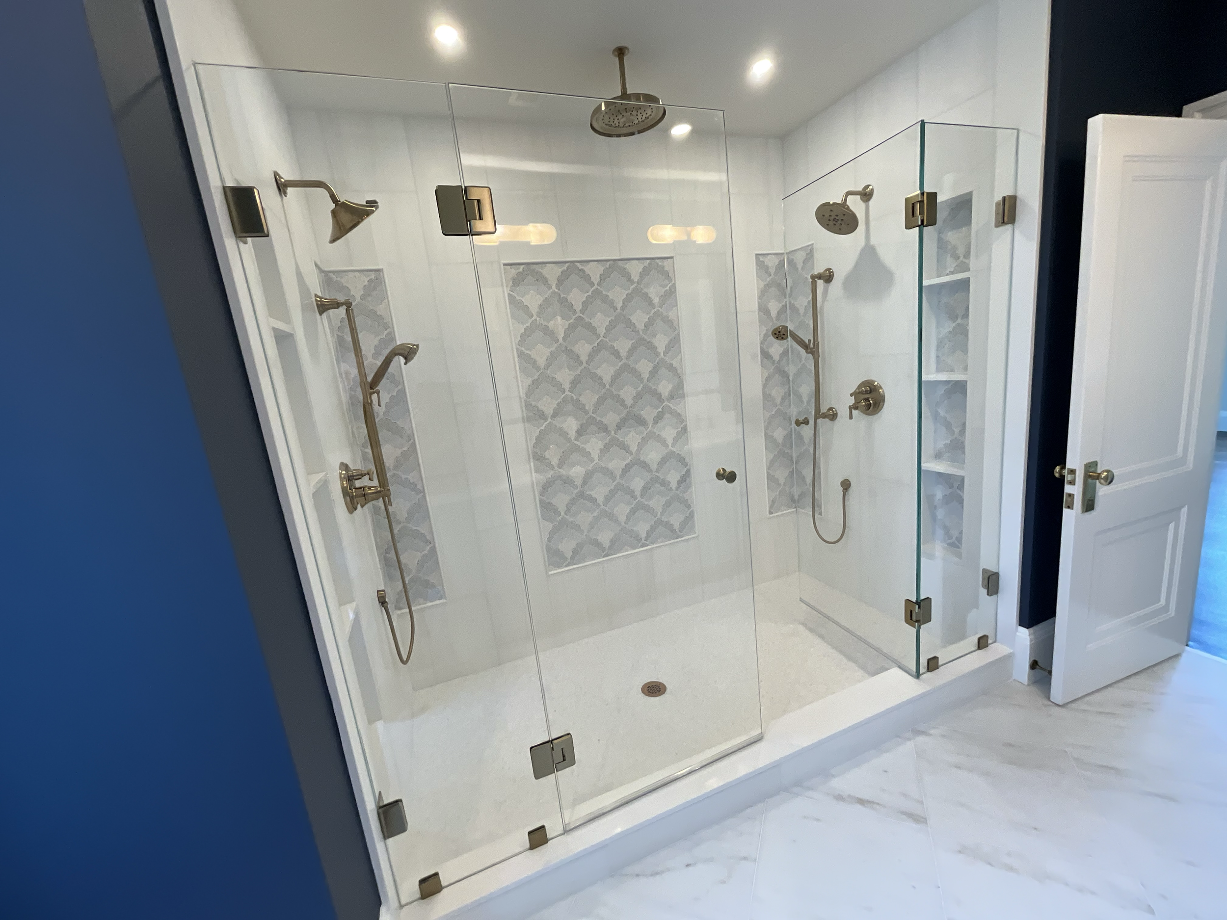 A modern walk-in shower with glass walls, multiple showerheads, and decorative tile accents.