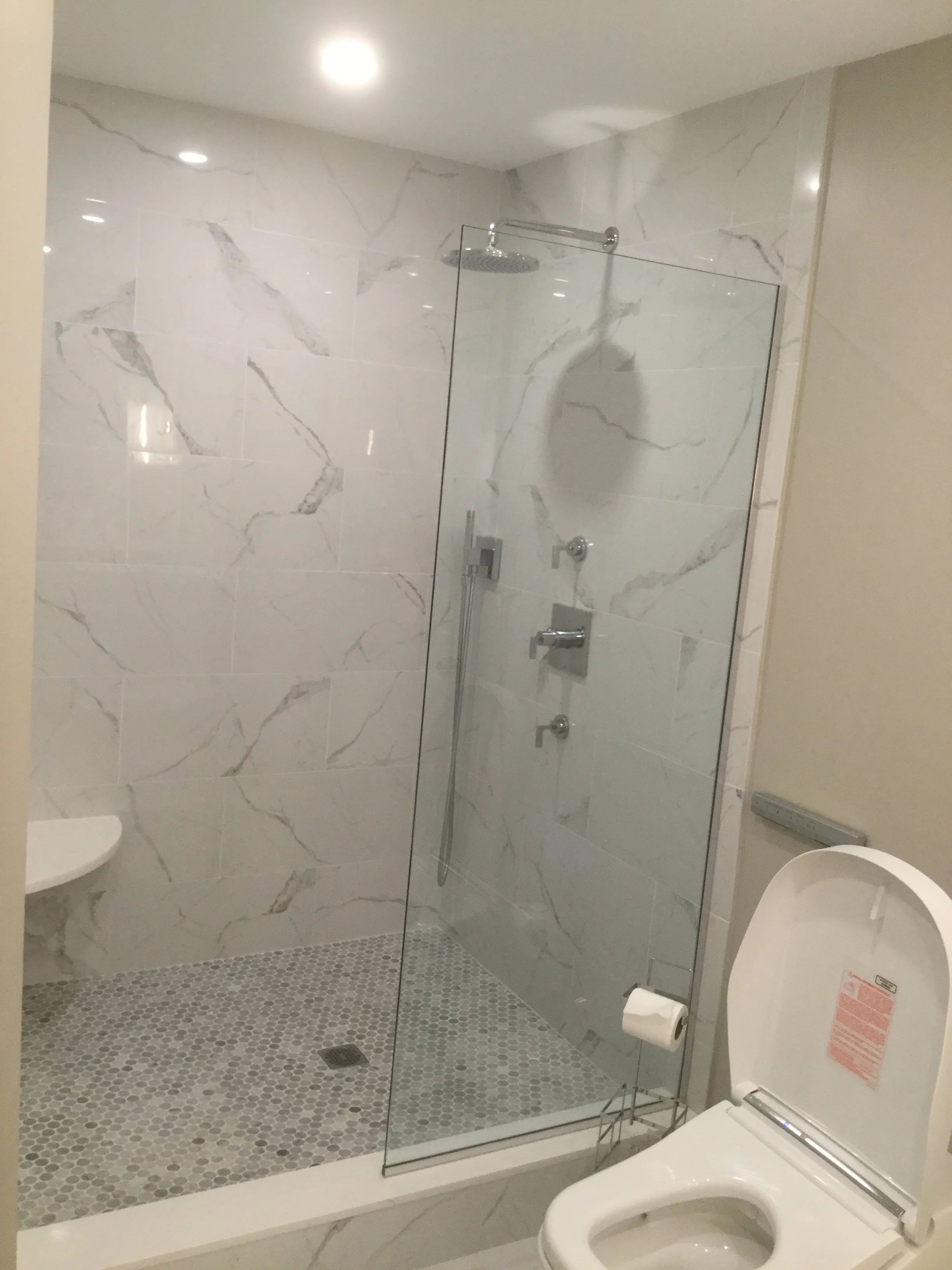 Modern bathroom with marble walls, glass shower enclosure, and a white toilet.