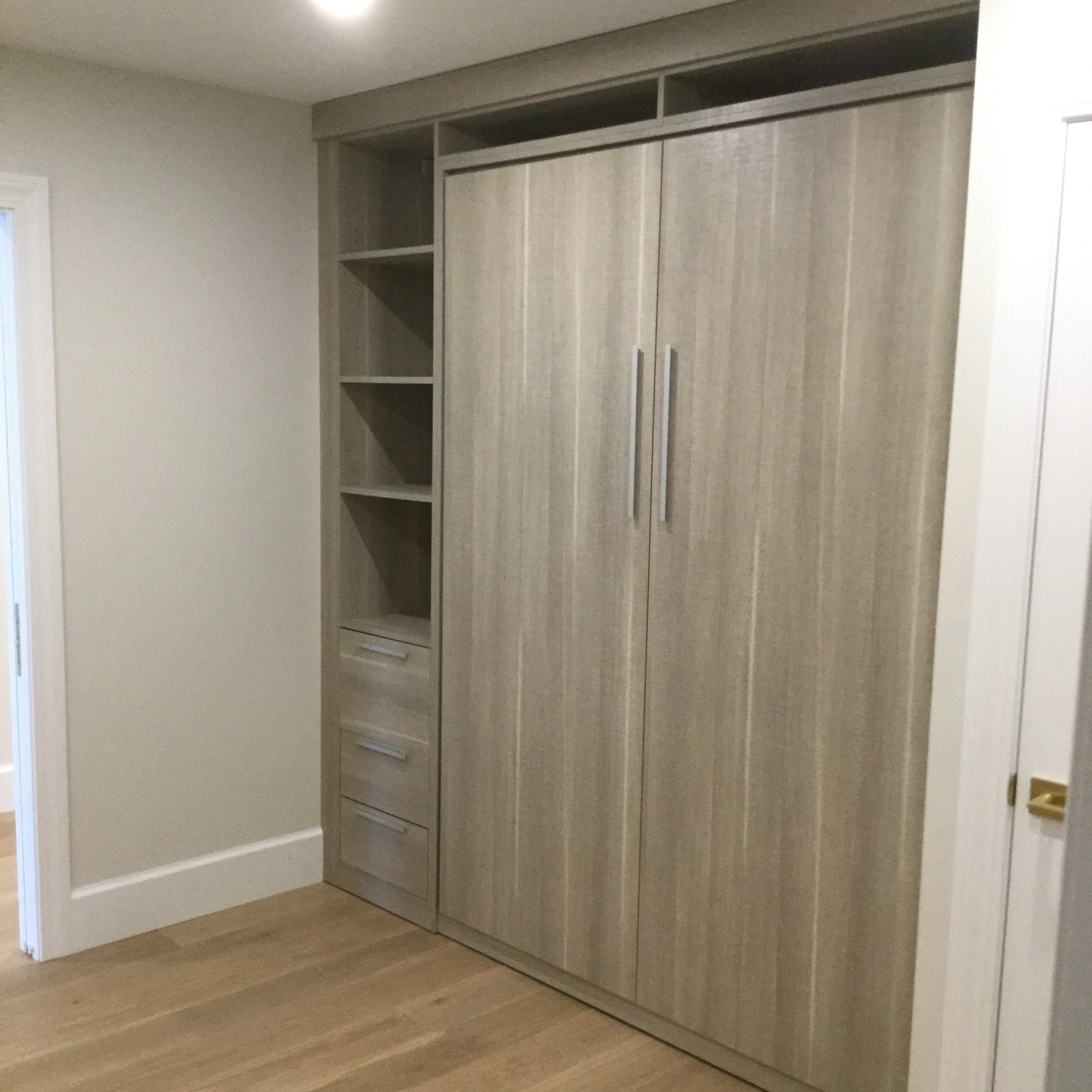 Built-in closet with sliding doors, open shelves, and drawers inside a room with light-colored walls and wooden flooring.