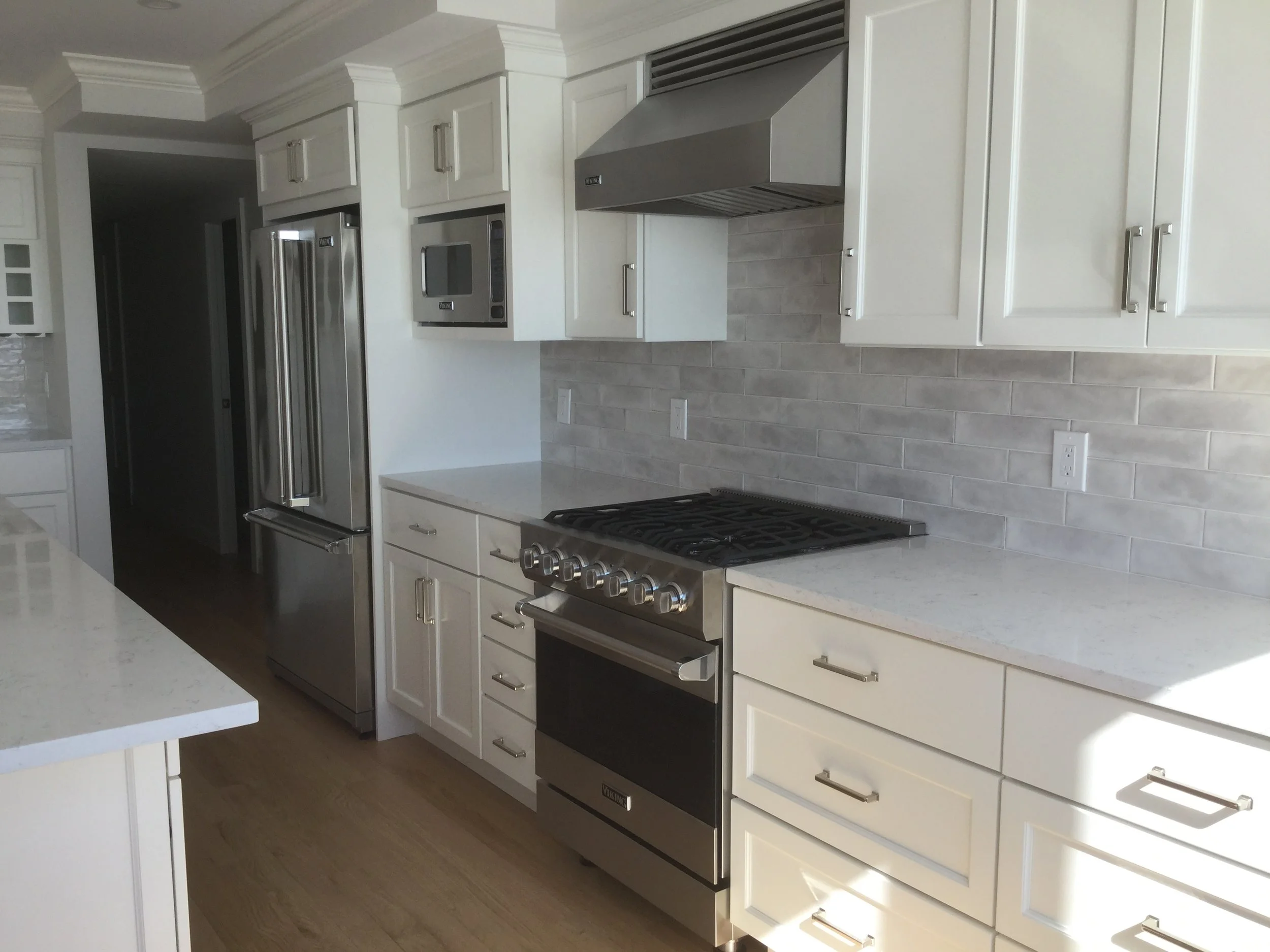 Modern kitchen with white cabinets, stainless steel refrigerator, microwave, and oven, light-colored countertop, and wood flooring.